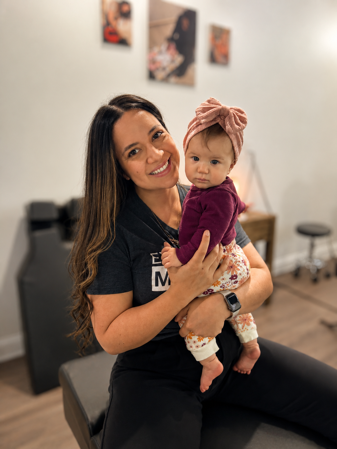 A woman holding a baby girl in an indoor setting with wall art in the background.