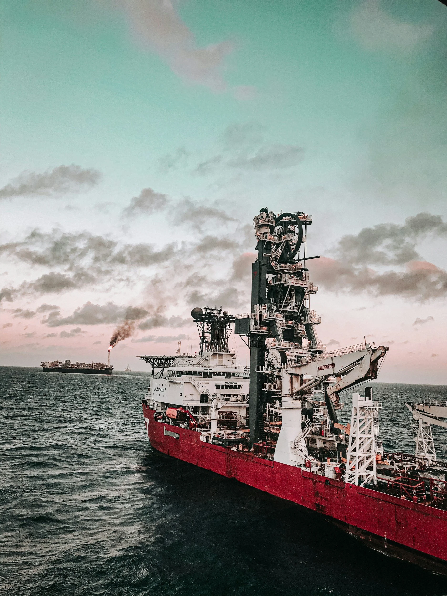 Un grand navire de production pétrolière en mer avec un autre navire en arrière-plan, au coucher du soleil, dans une mer calme.