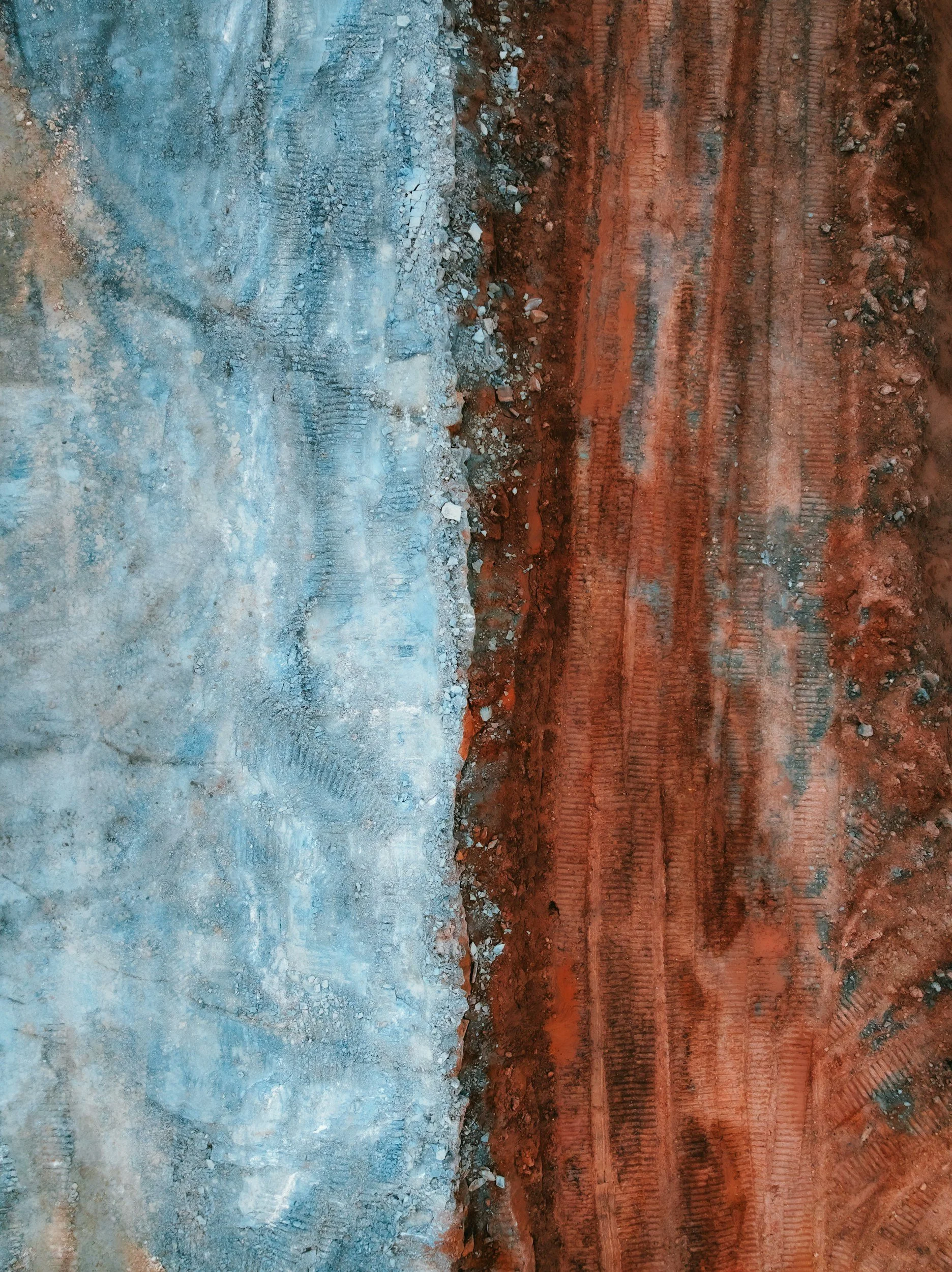Une vue de deux surfaces de sol ou de terrain, l'une en terre rouge avec des traces de pneus ou de chevauchements, l'autre en surface plus pierreuse ou sablonneuse, séparées par un petit dénivelé.