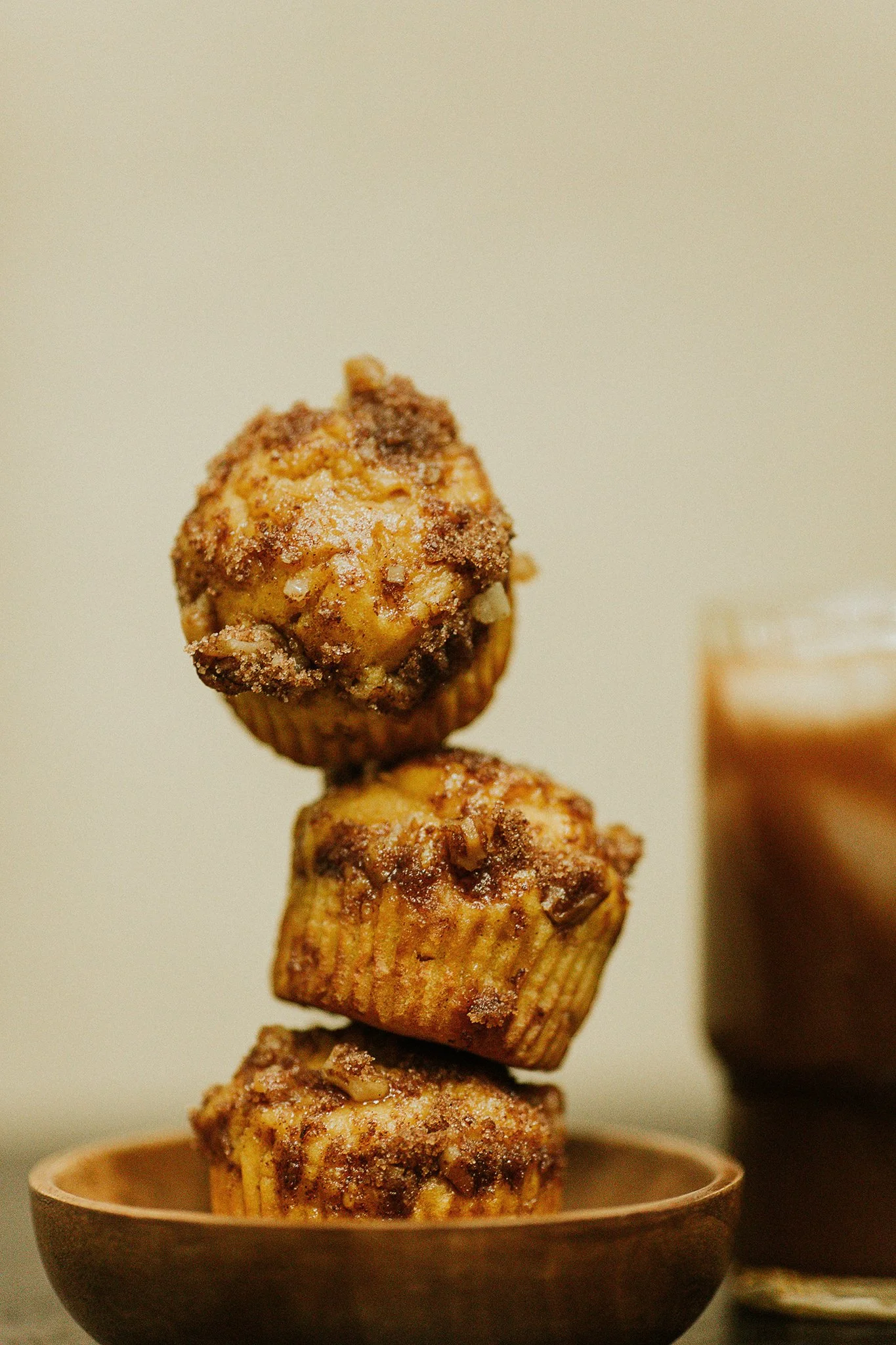 Stack of four muffin-like treats with a crumbly topping, placed in a brown bowl.