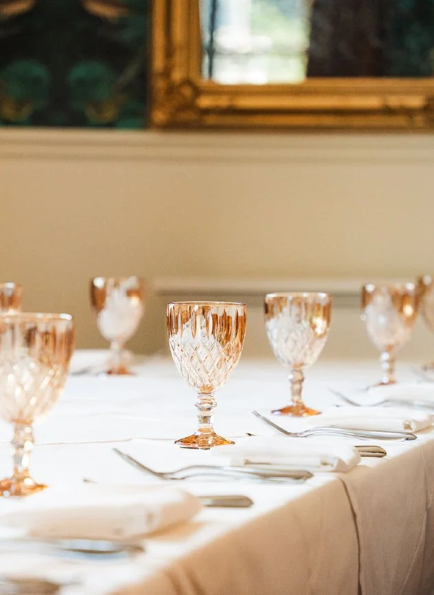 Elegant dining table set with pink glassware and white napkins, with a mirror and framed artwork in the background.