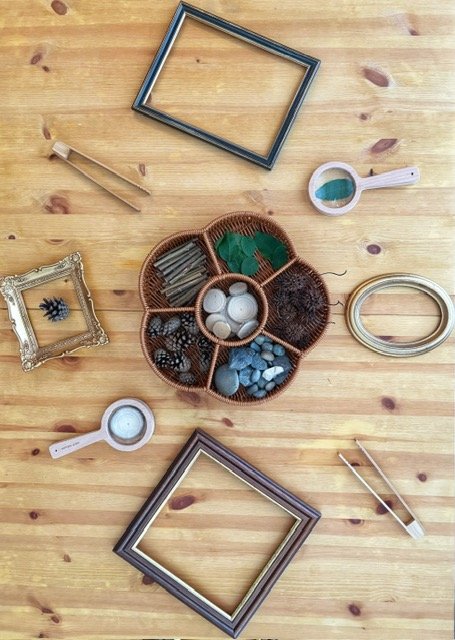 Flat lay of picture frames, a wicker jewelry or trinket tray, small magnifying glasses, and decorative items arranged on a wooden surface.