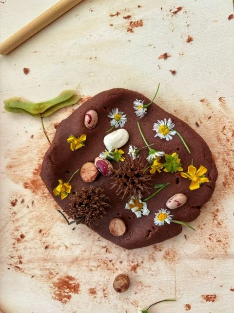 A scattered pile of chocolate clay with flowers, mini eggs, and small nuts on a white surface.
