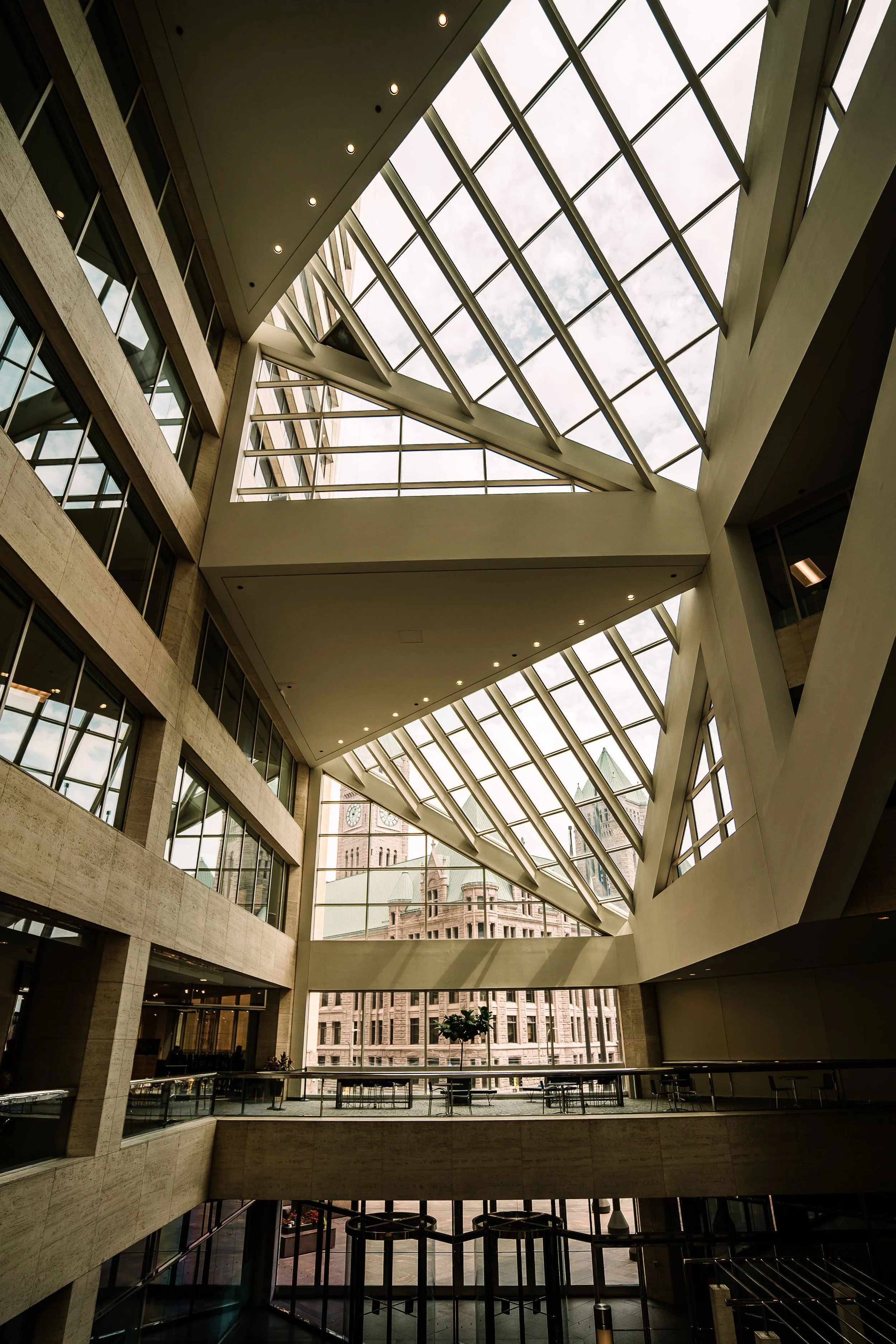 Interior view of a modern building with multiple floors, featuring large glass windows and a geometric glass ceiling allowing natural light.