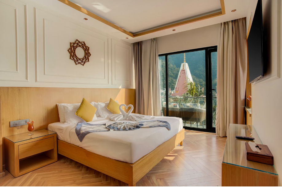 A hotel room with a large bed decorated with swan towel art, pillows, and a view of a temple with a mountain backdrop through sliding glass doors.