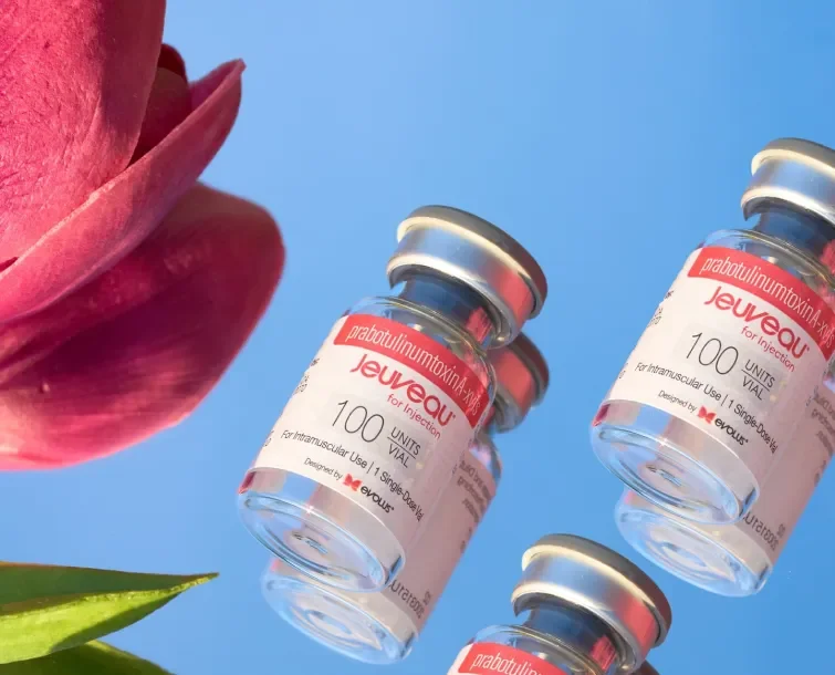 Three vials of Juevesque vaccines floating in the air against a blue background, with a pink flower and green leaf partially visible.