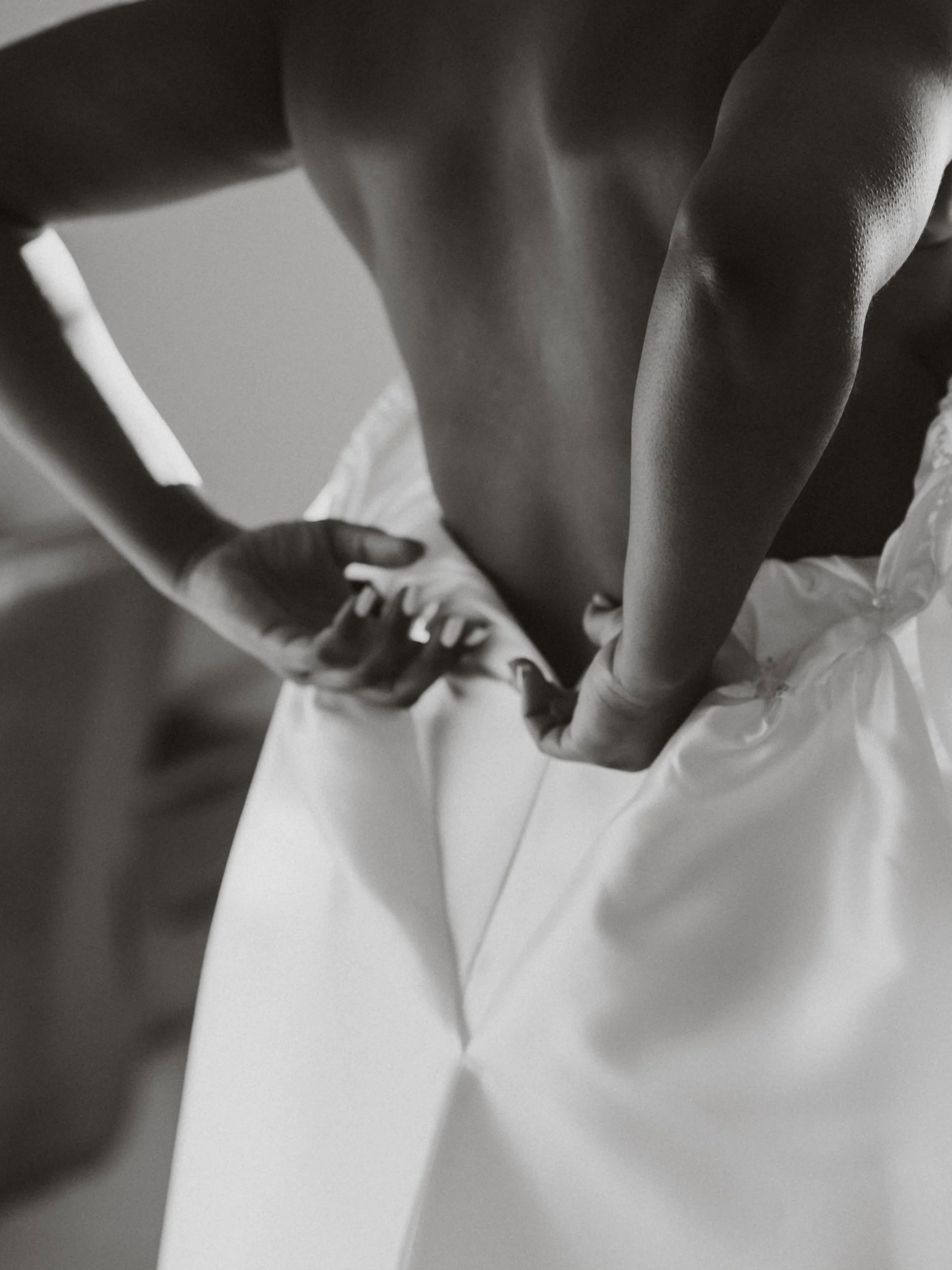 A close-up black and white photo of a person with a medium skin tone, holding a piece of paper or fabric, with part of their body visible.