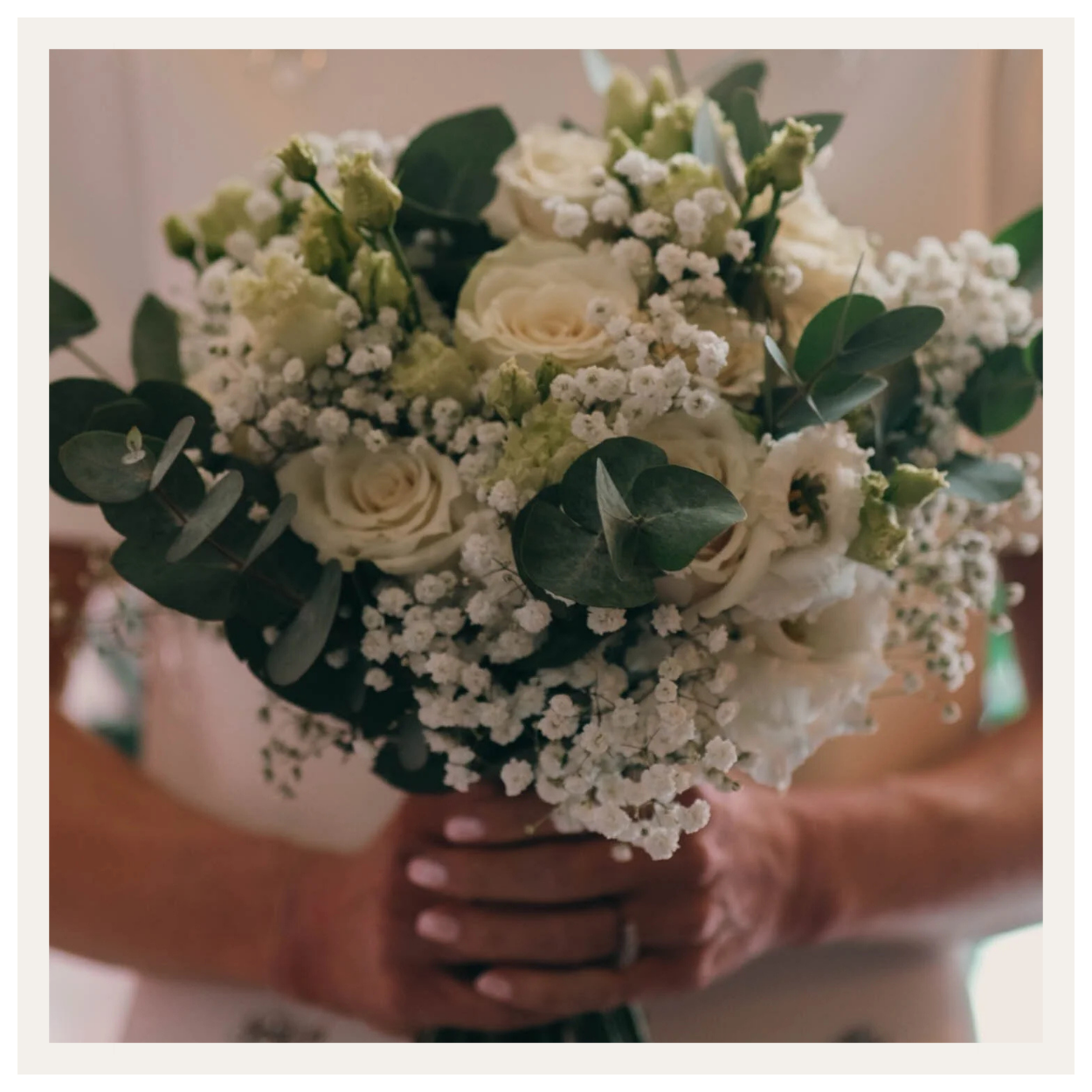 A person holding a bouquet of white roses, baby's breath, and eucalyptus leaves.