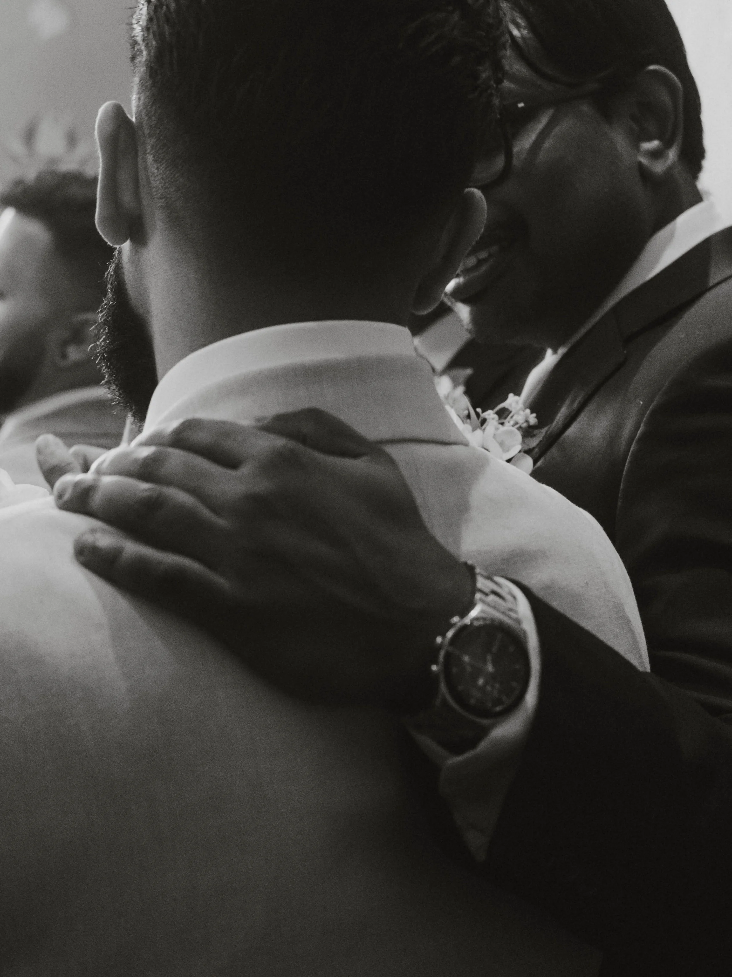 Two men sharing a joyful moment, close embrace, both wearing formal suits, one with glasses, black and white photo.