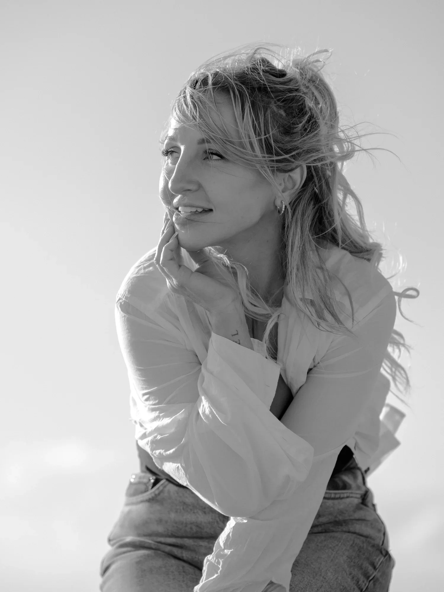 Black and white photo of a woman with curly hair smiling and looking to the side, wearing a light-colored shirt and jeans.
