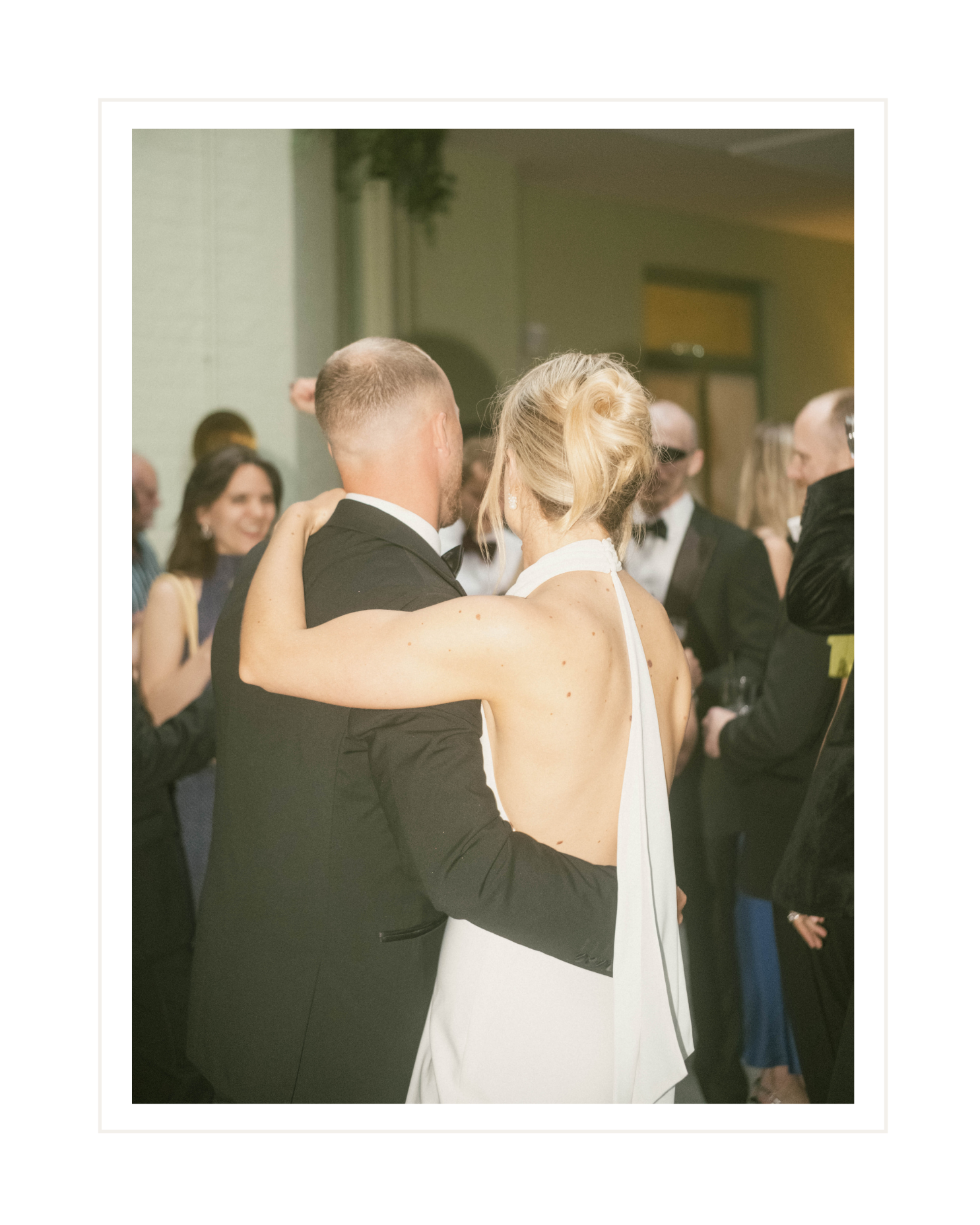 A couple dancing closely at a formal event, surrounded by other well-dressed attendees.
