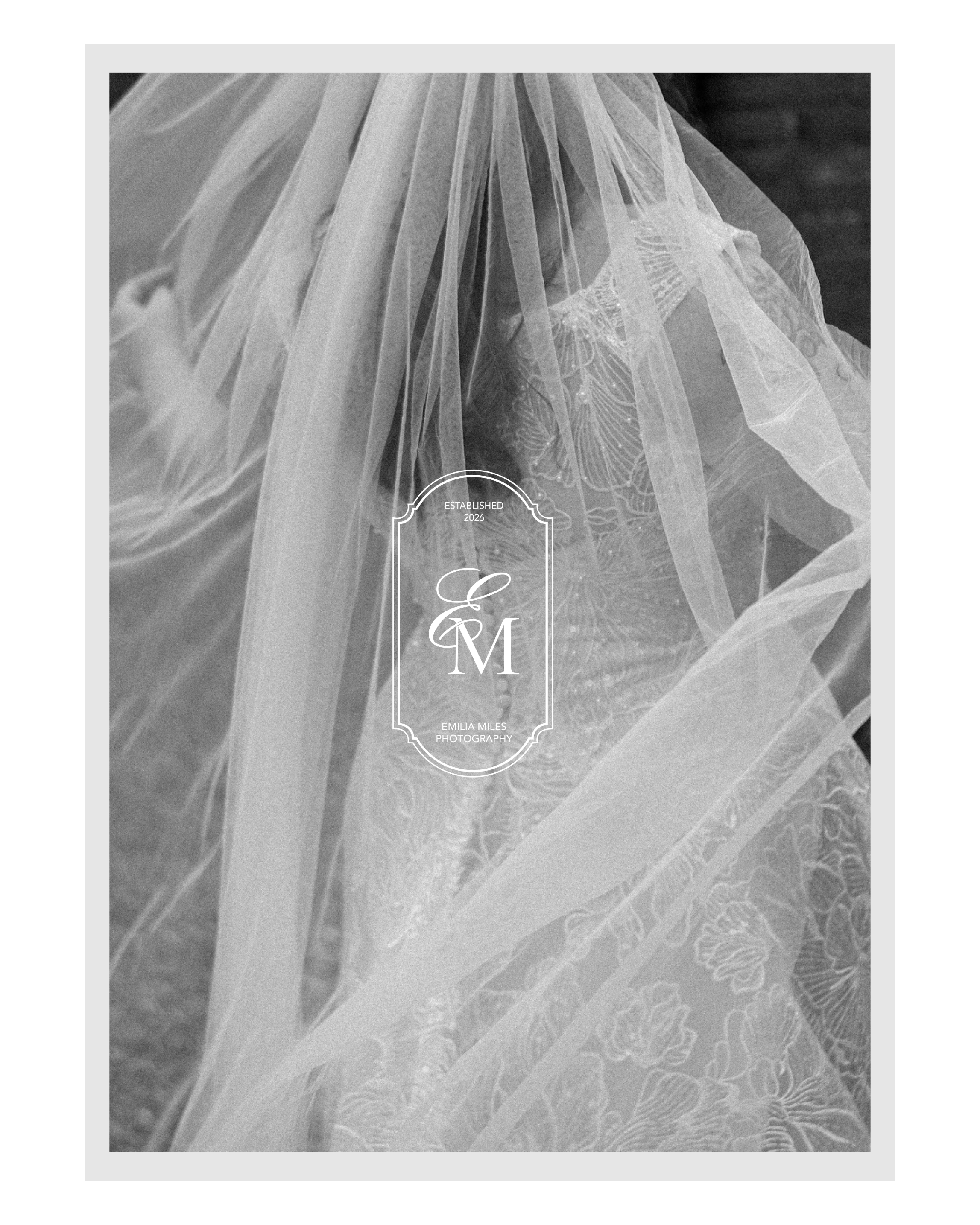 A black and white photograph of wedding dress fabric with a watermark label displaying the initials 'E & M', established in 2026, and the name Emilia Miles Photography.