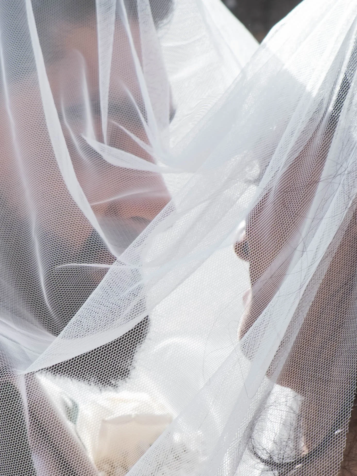 Close-up of a sheer white fabric with a fine mesh pattern, draped over a person's legs, creating a layered, textured appearance.