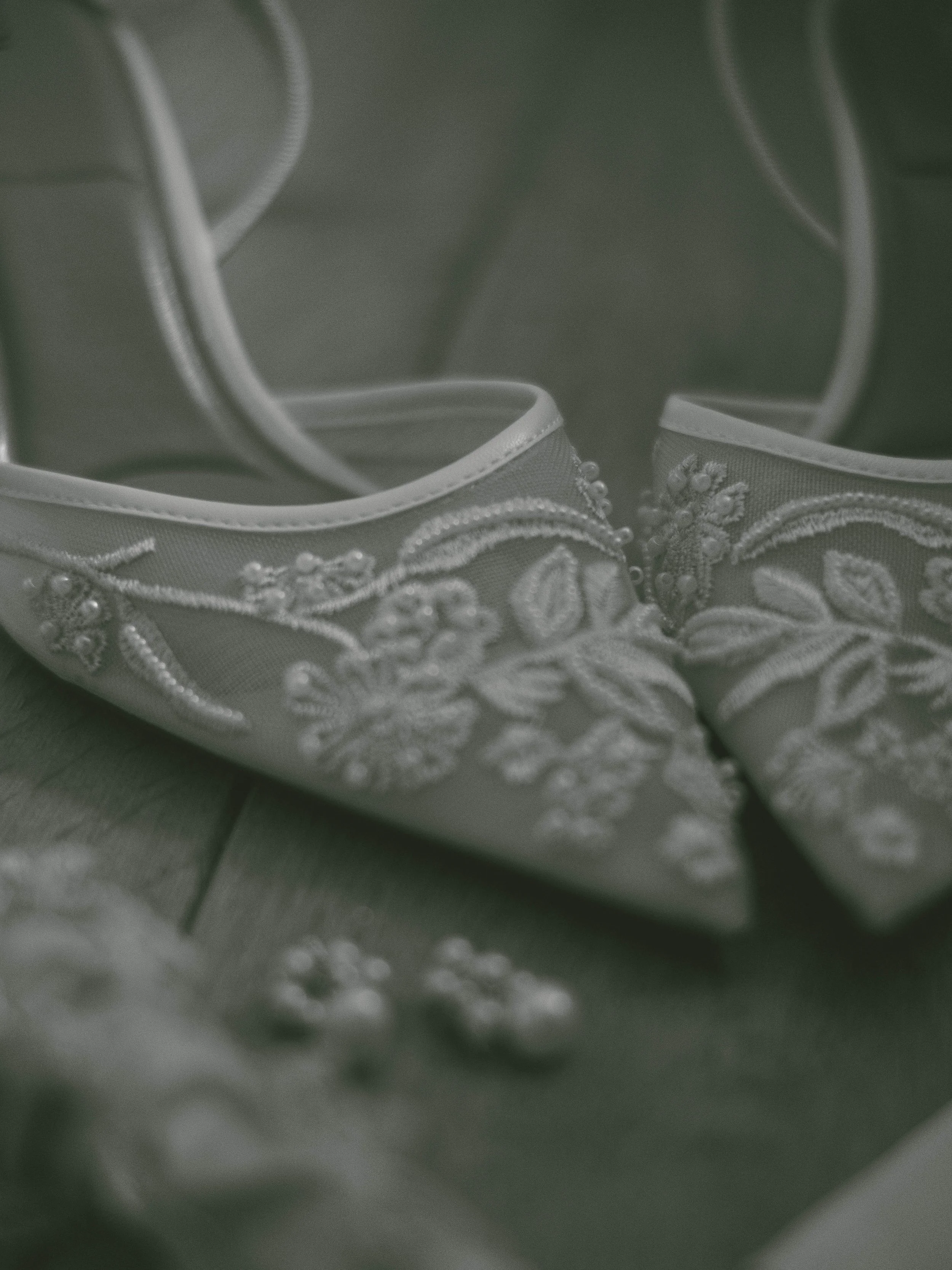 Close-up of white satin heels with embroidery and beadwork, positioned side by side.