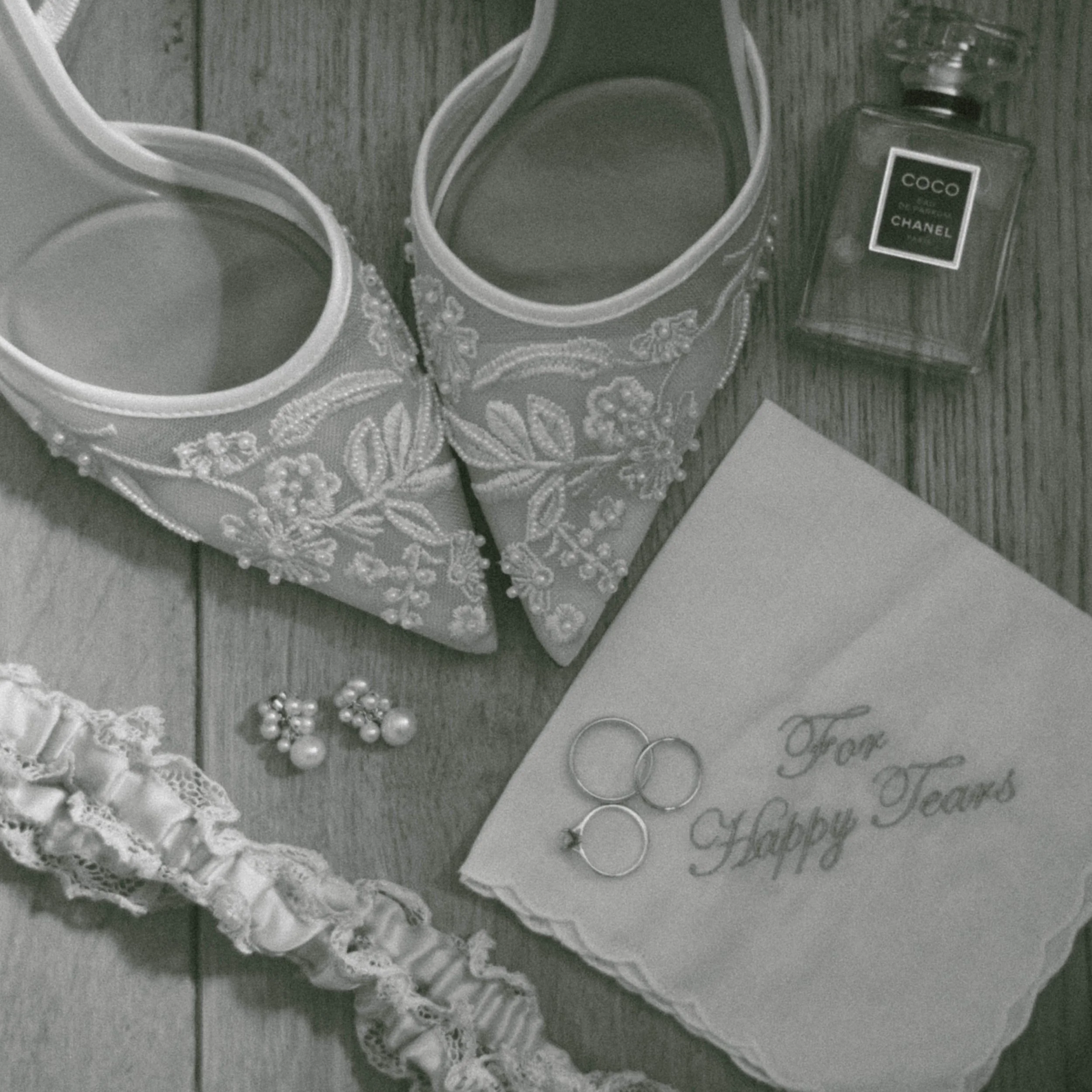 A collection of jewelry, including rings, earrings, and a pearl bracelet, arranged on a decorative cloth and a piece of paper with handwritten words. There is also a small bottle of Chanel Coco perfume nearby.