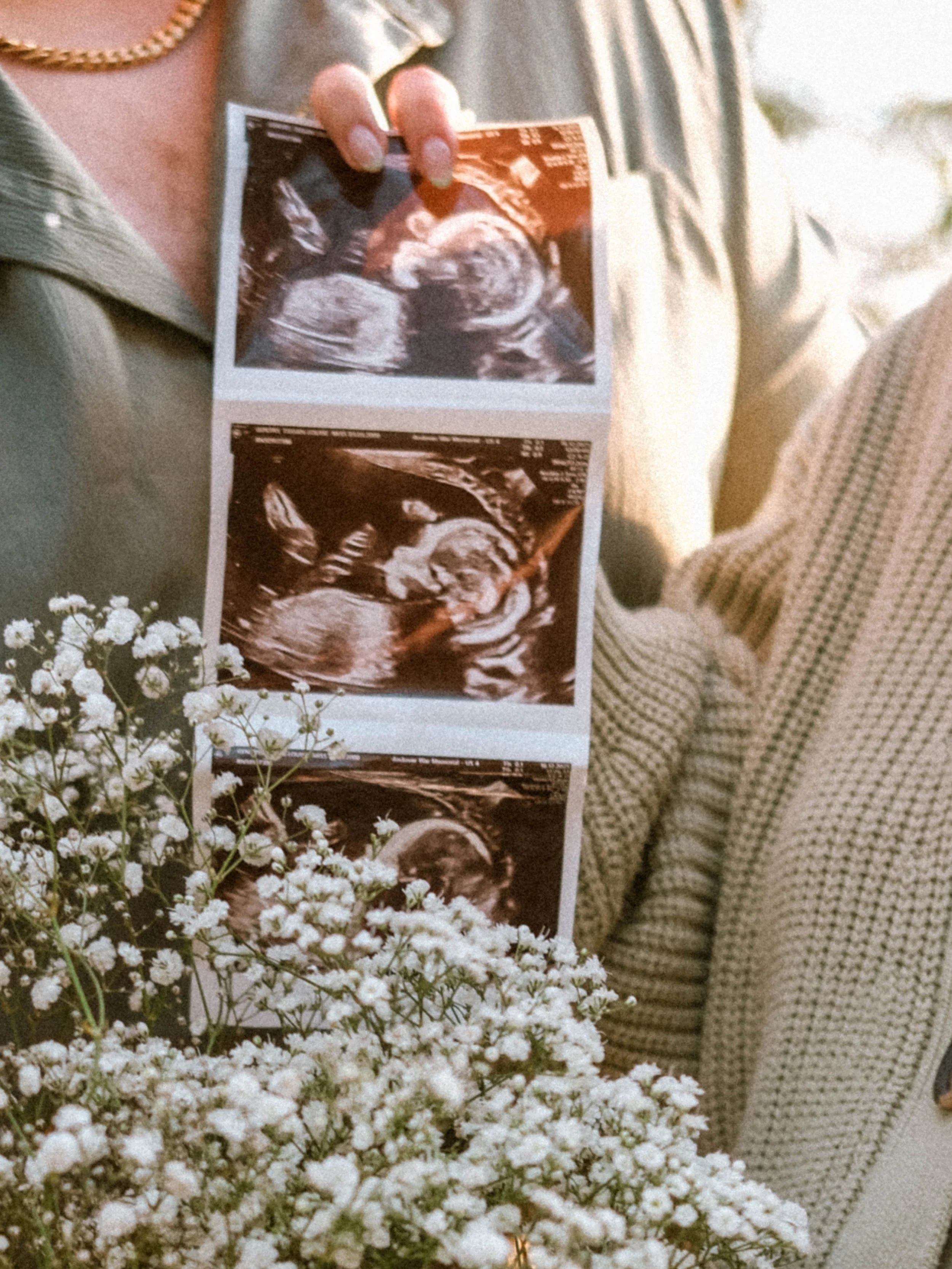 A person holding ultrasound images of a baby near a bouquet of white flowers.