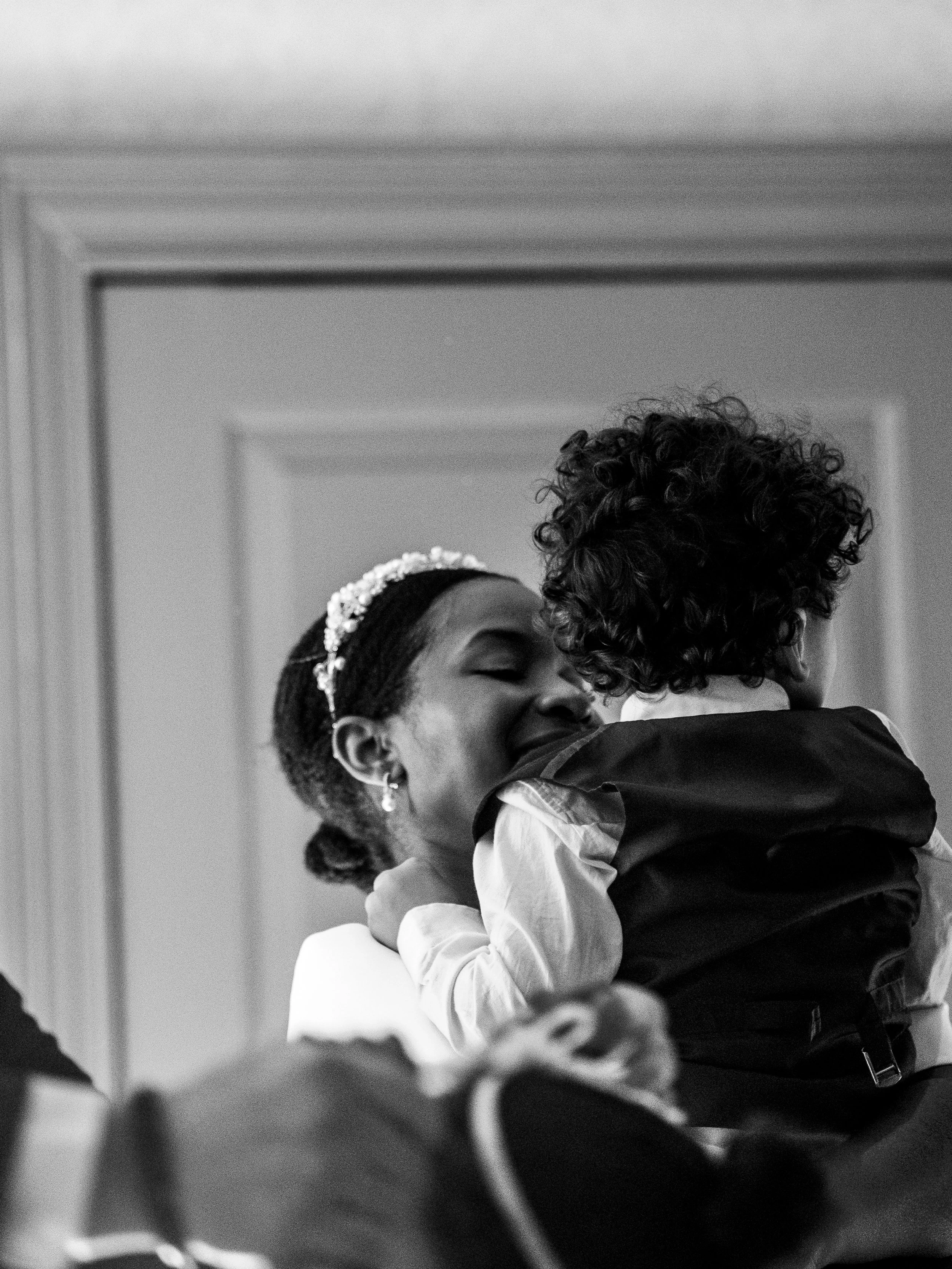 A woman with a floral headband hugging a young boy with curly hair in an indoor setting.