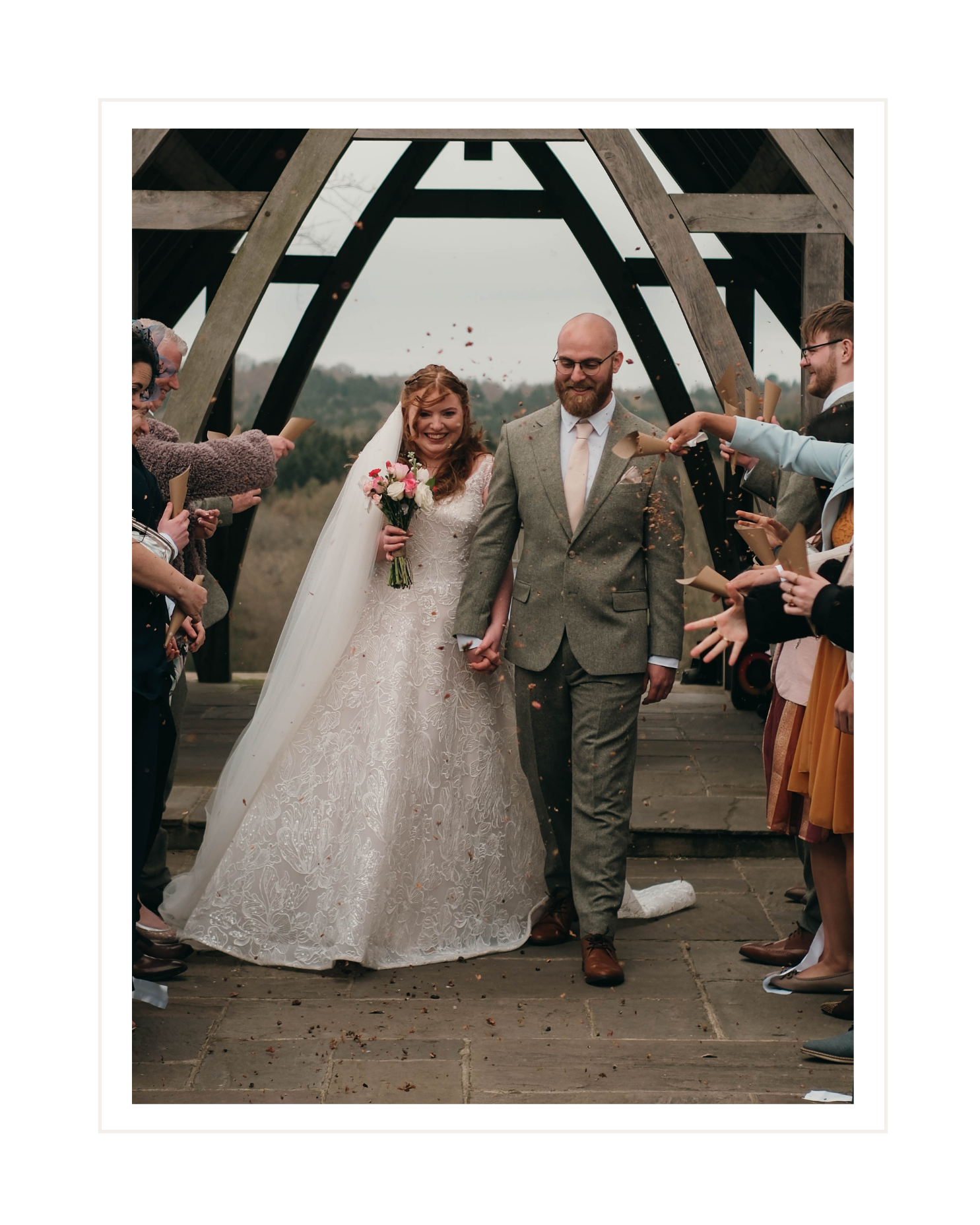 A bride and groom walking hand in hand outdoors during their wedding celebration, surrounded by guests throwing confetti.