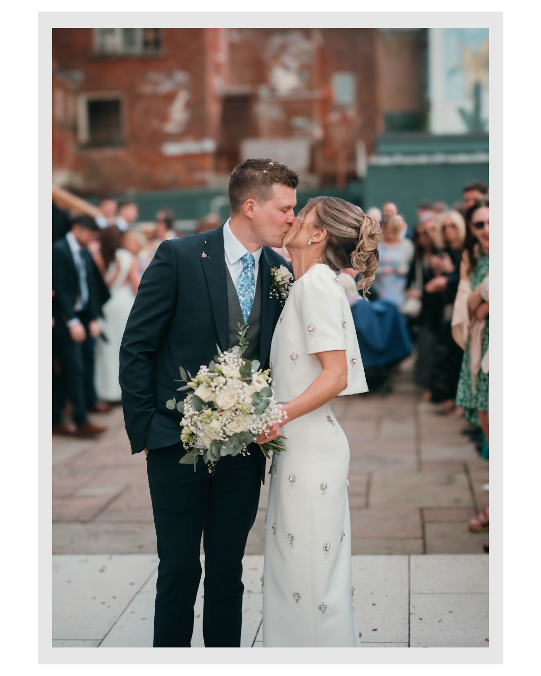A bride and groom share a kiss during their wedding ceremony, with guests in the background.