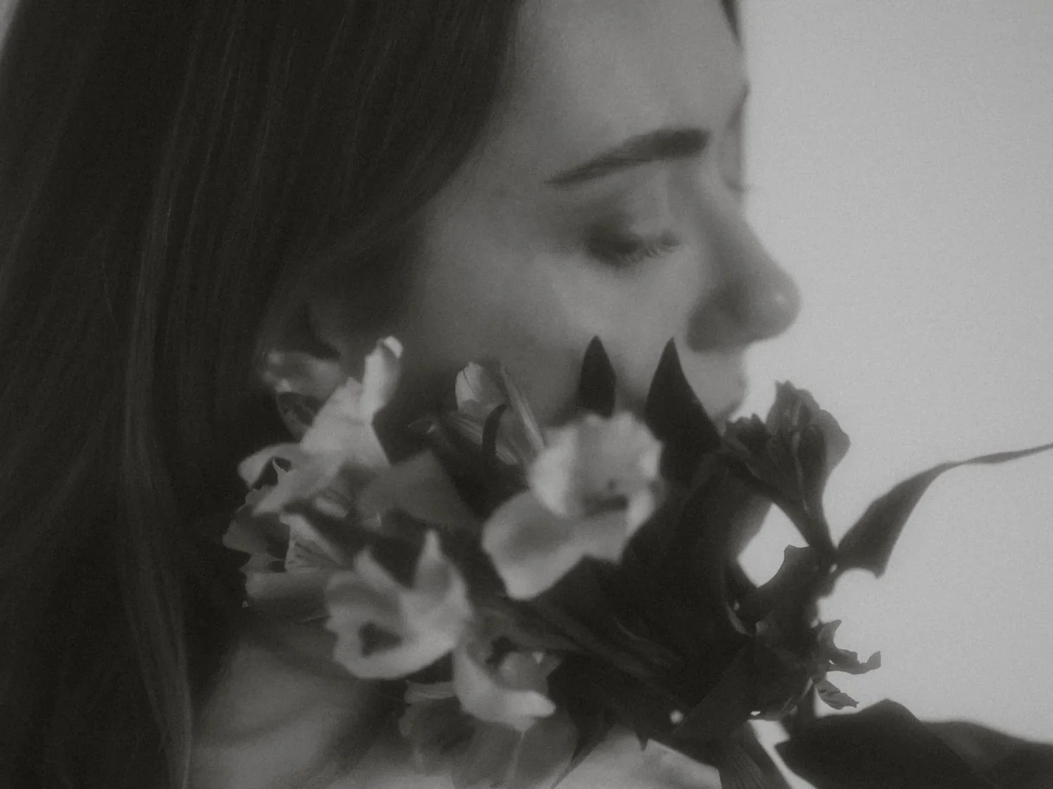 A grayscale photo of a woman with closed eyes holding a large bouquet of flowers close to her face.