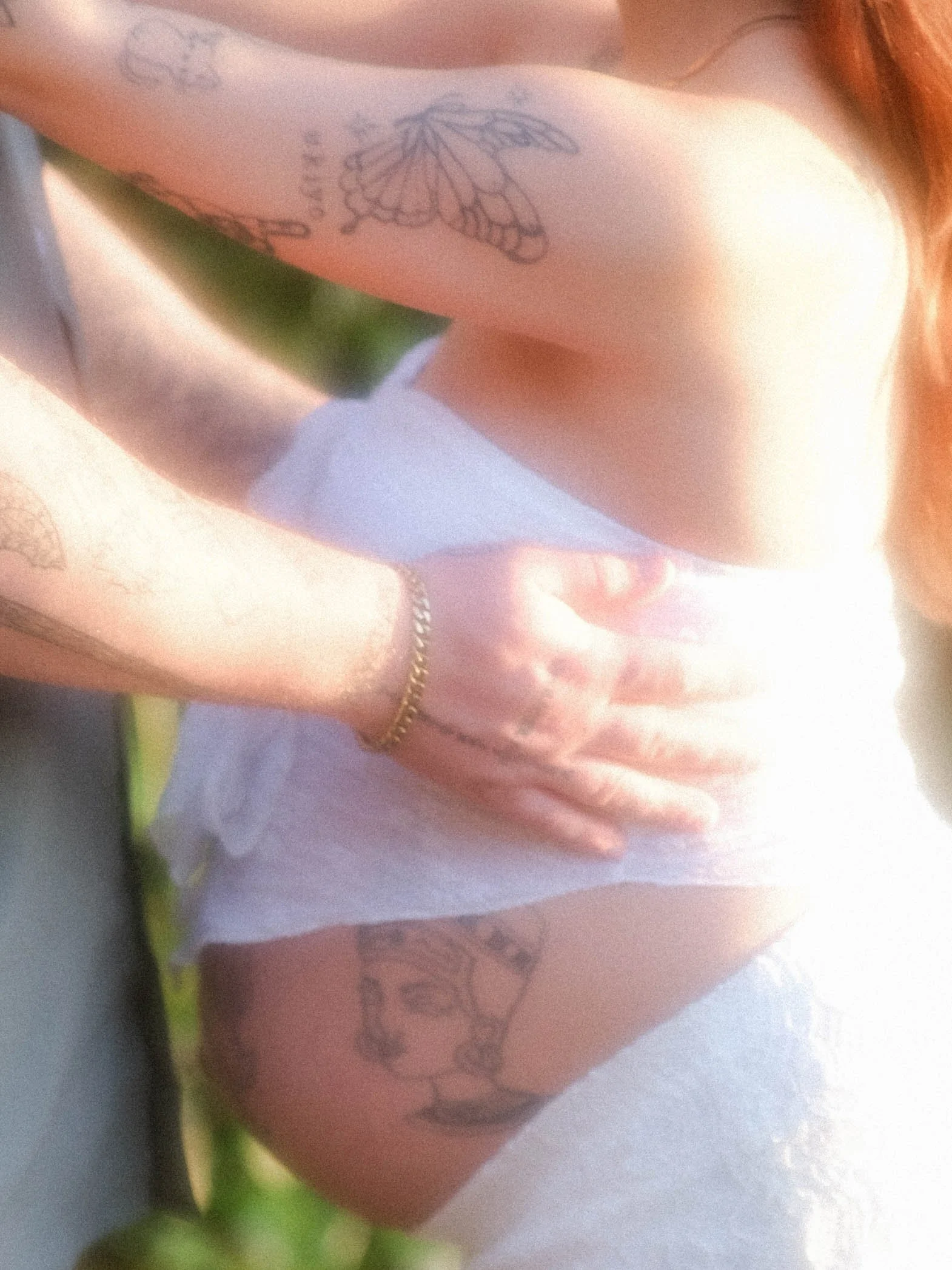 Close-up of a person's torso with tattoos of butterflies and other designs, wearing white underwear and a gold chain necklace.