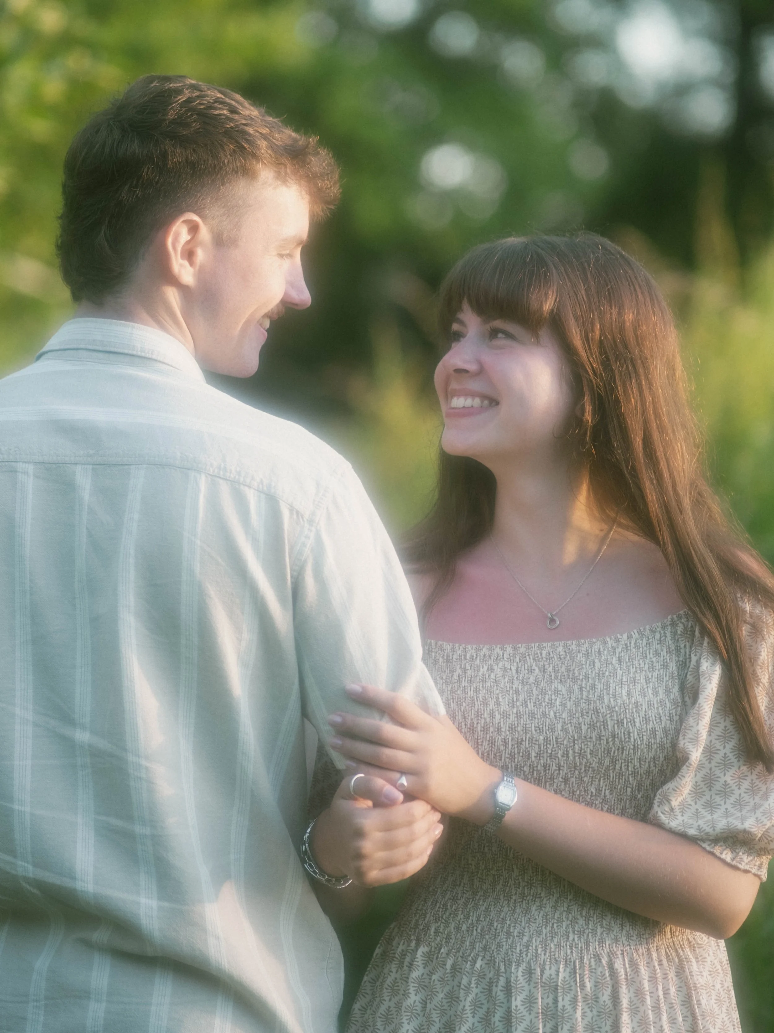 A couple holding hands and smiling at each other outdoors during daylight.