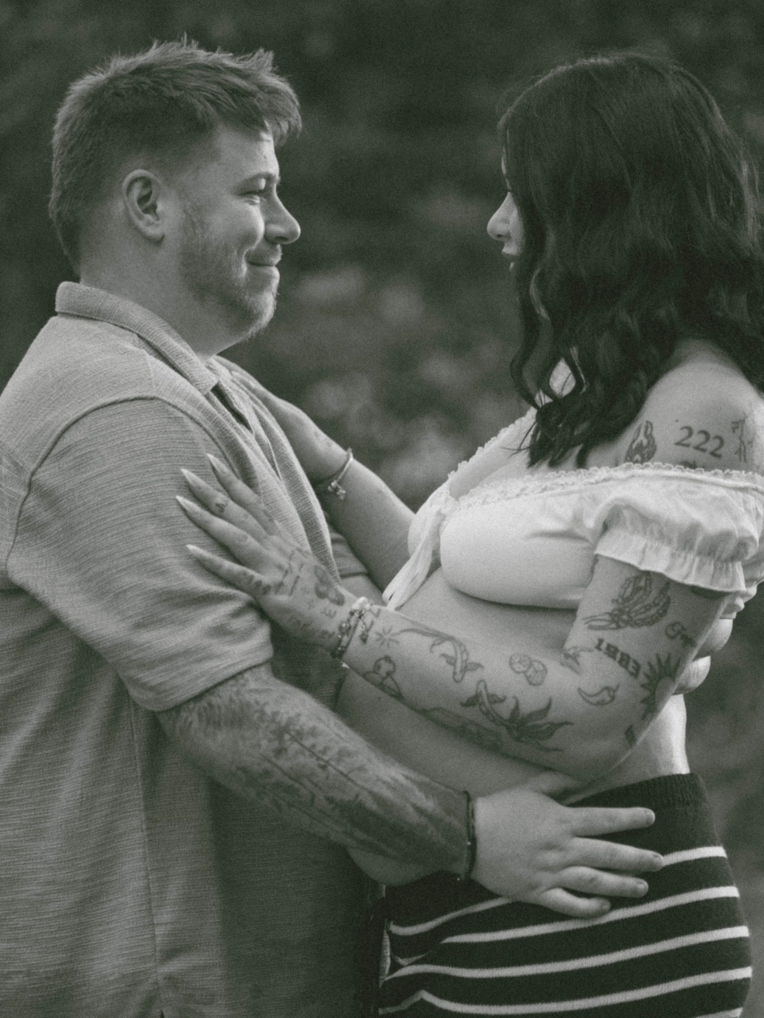 A black and white photo of a man and woman facing each other, smiling, with the woman cradling her stomach, indicating pregnancy.