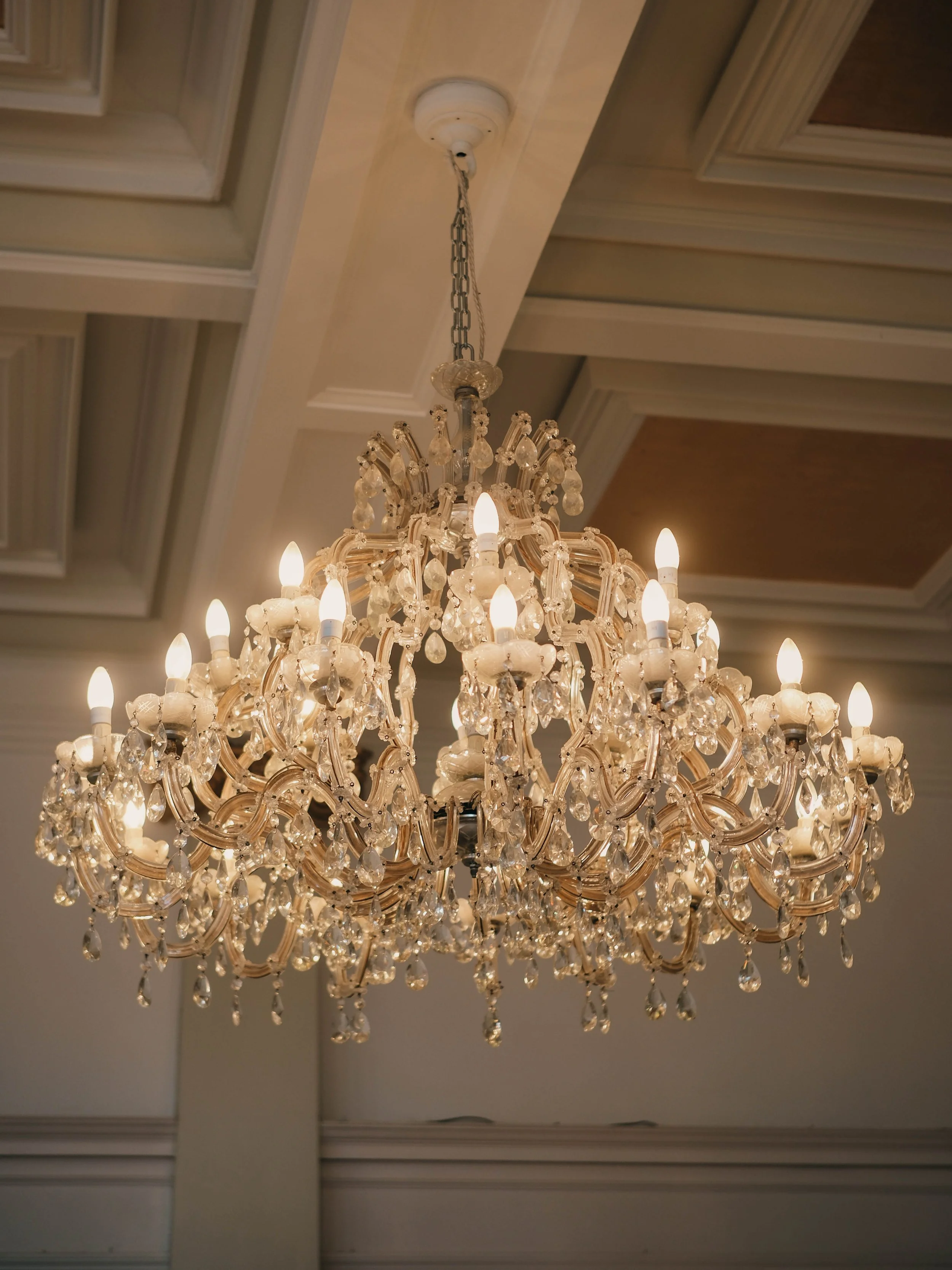 Elegant chandelier with multiple lit bulbs and hanging decorative crystals, suspended from a ceiling with intricate molding.