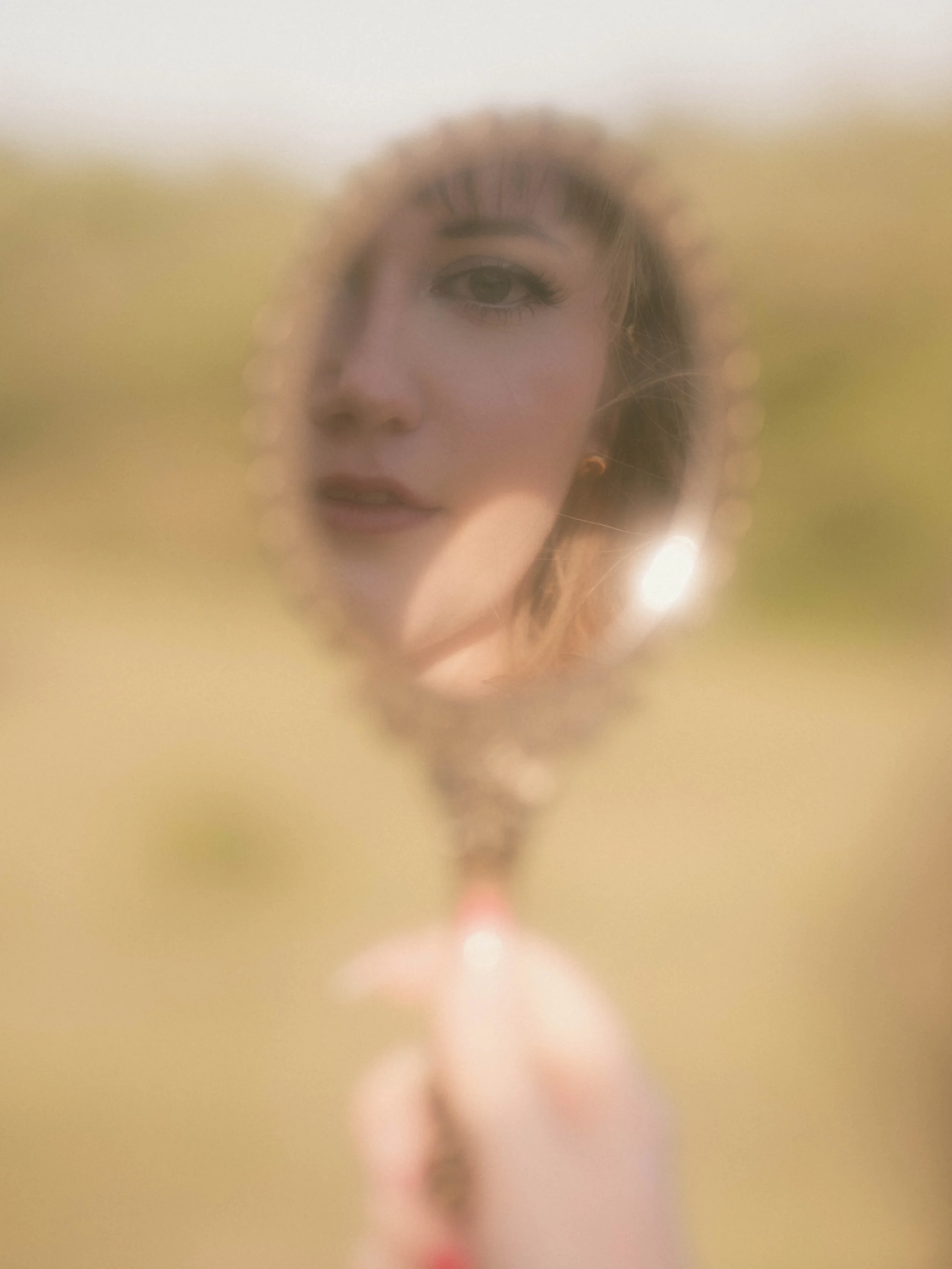 A blurry portrait of a woman with makeup and earrings, viewed through a foggy or frosted glass surface.