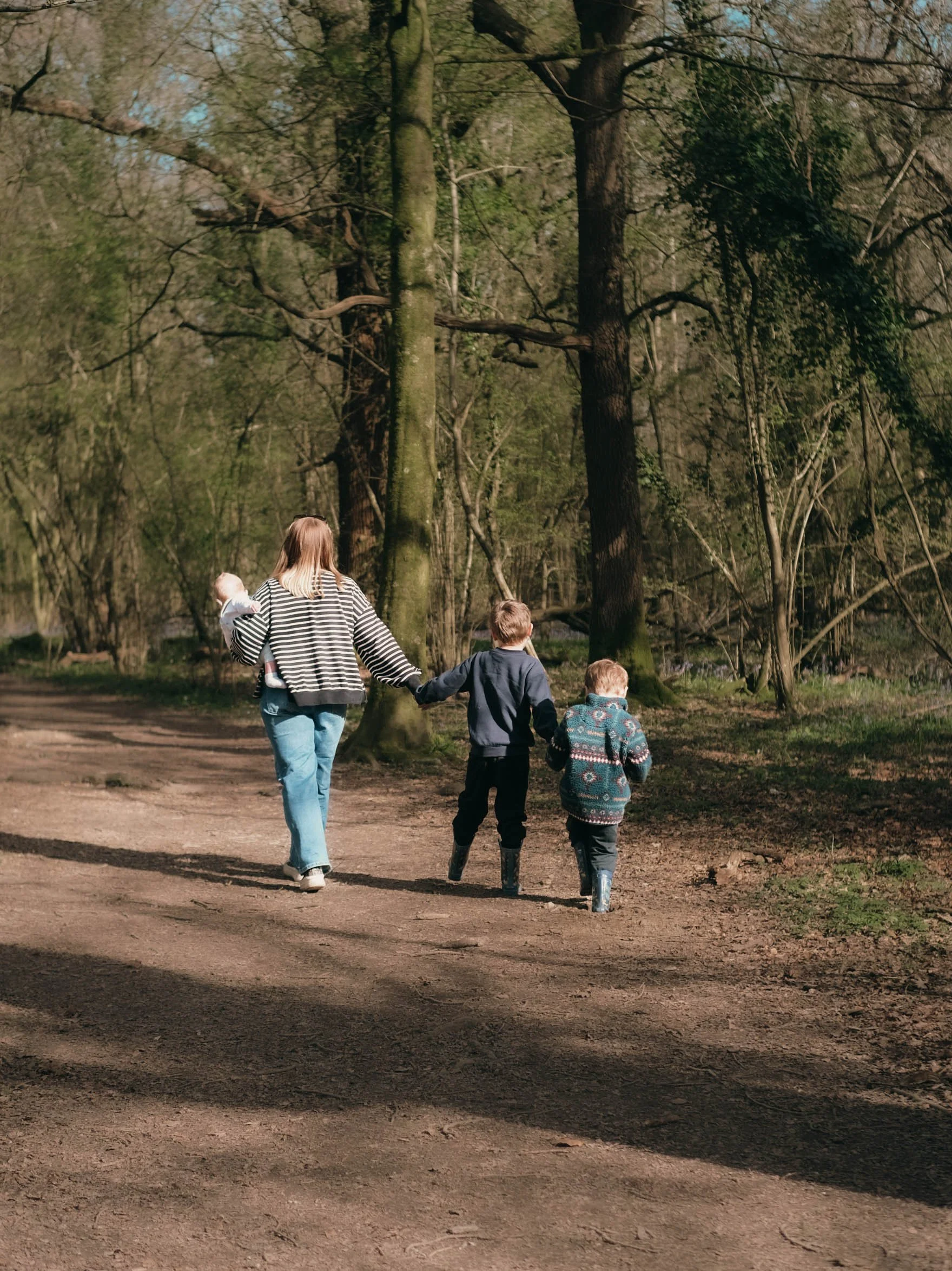 A woman and three children walking on a dirt path in a forest with trees and greenery.