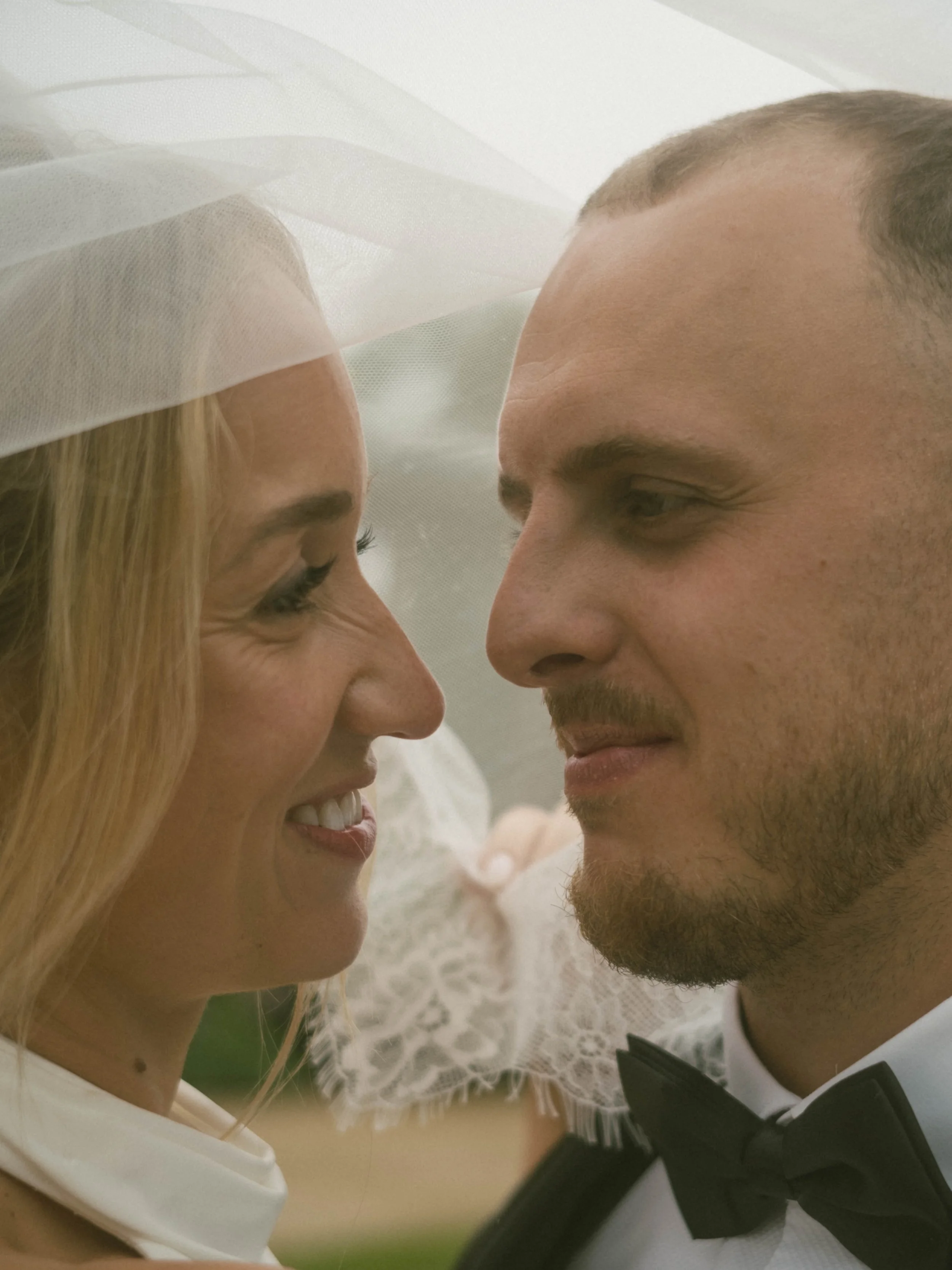 Close-up of a bride and groom with their foreheads touching, smiling, wedding attire, bride in a veil and dress, groom in tuxedo, soft focus background.