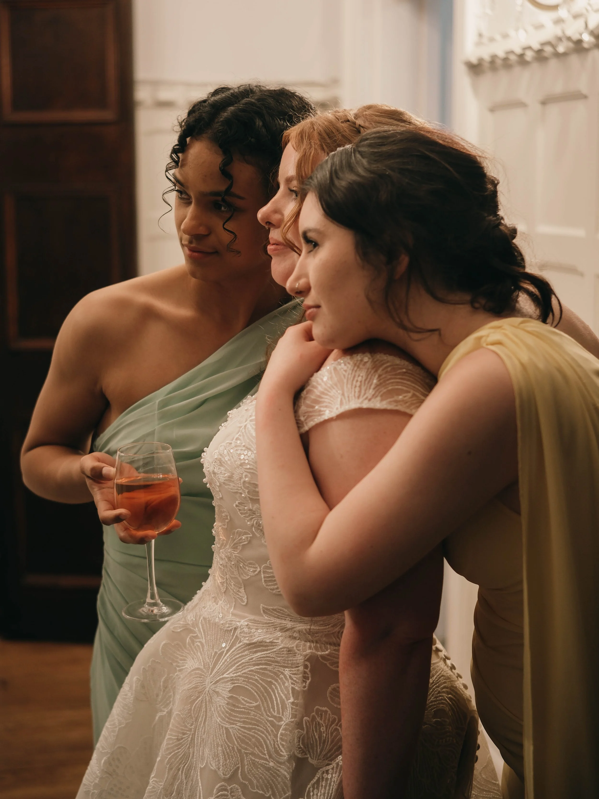 Three women sitting closely together at a social event, with one woman holding a glass of rosé wine.