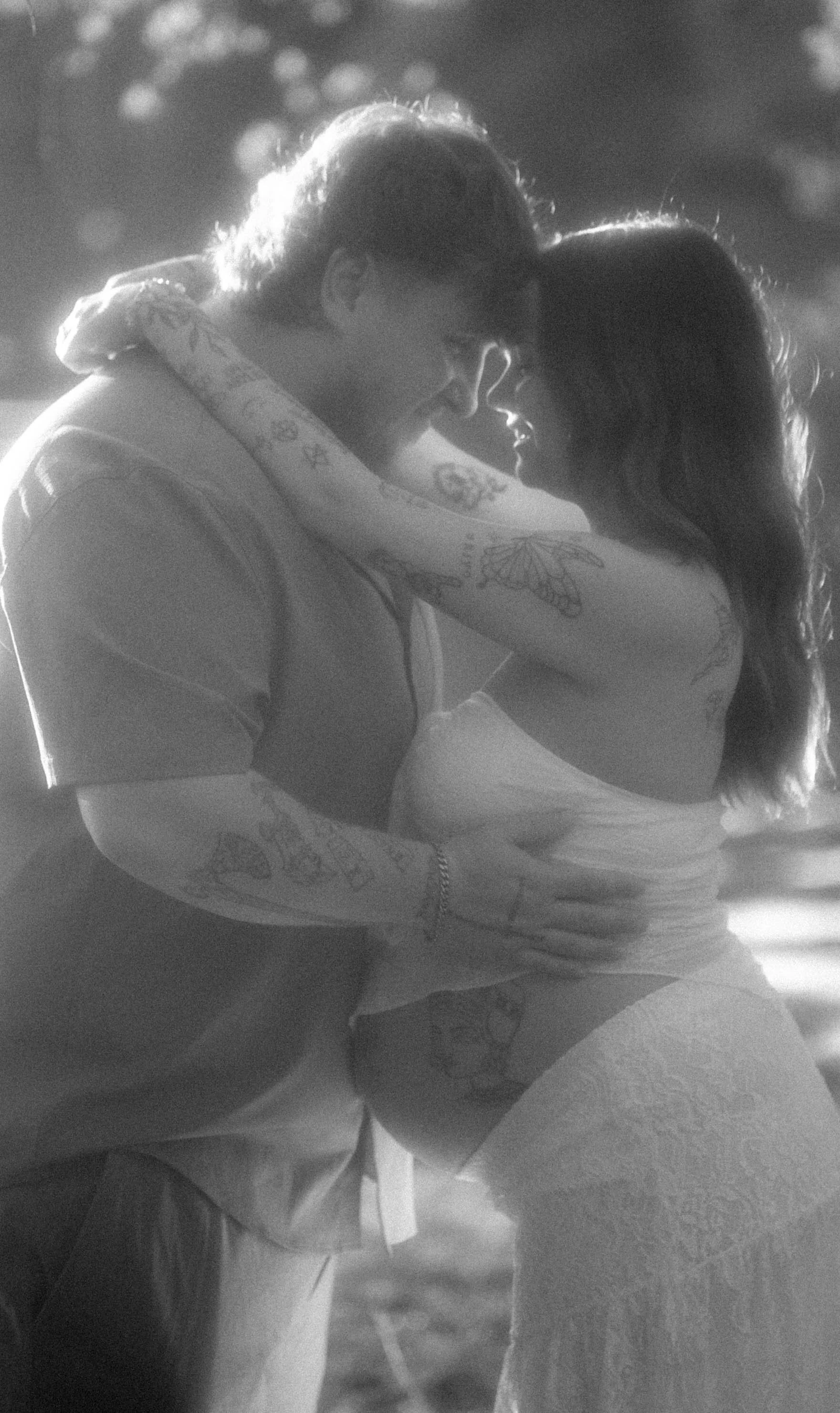 A black and white photo of a couple in an intimate embrace, forehead to forehead, with their eyes closed, sharing a tender moment.