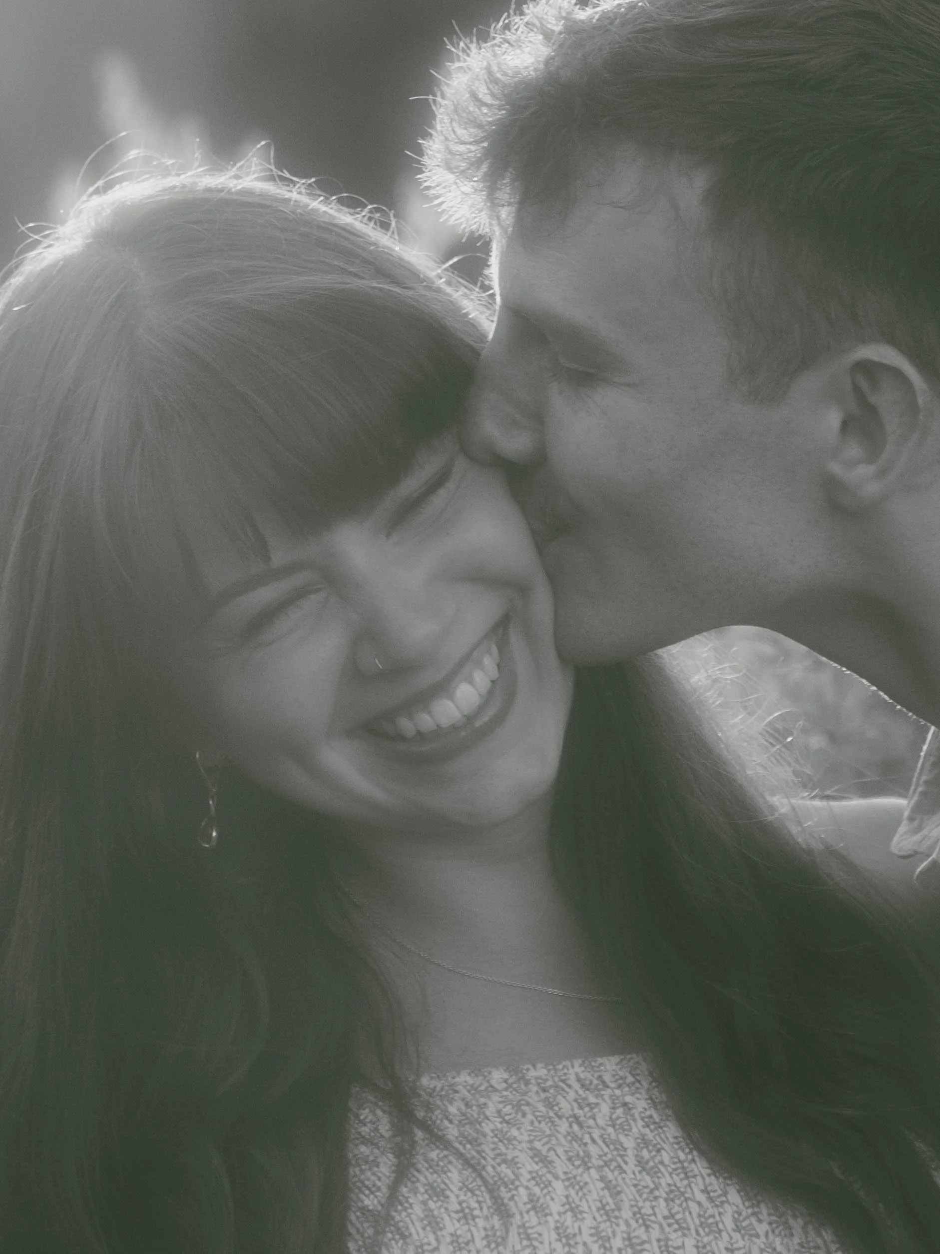 A man and a woman sharing a close, intimate moment, smiling, with their foreheads touching.