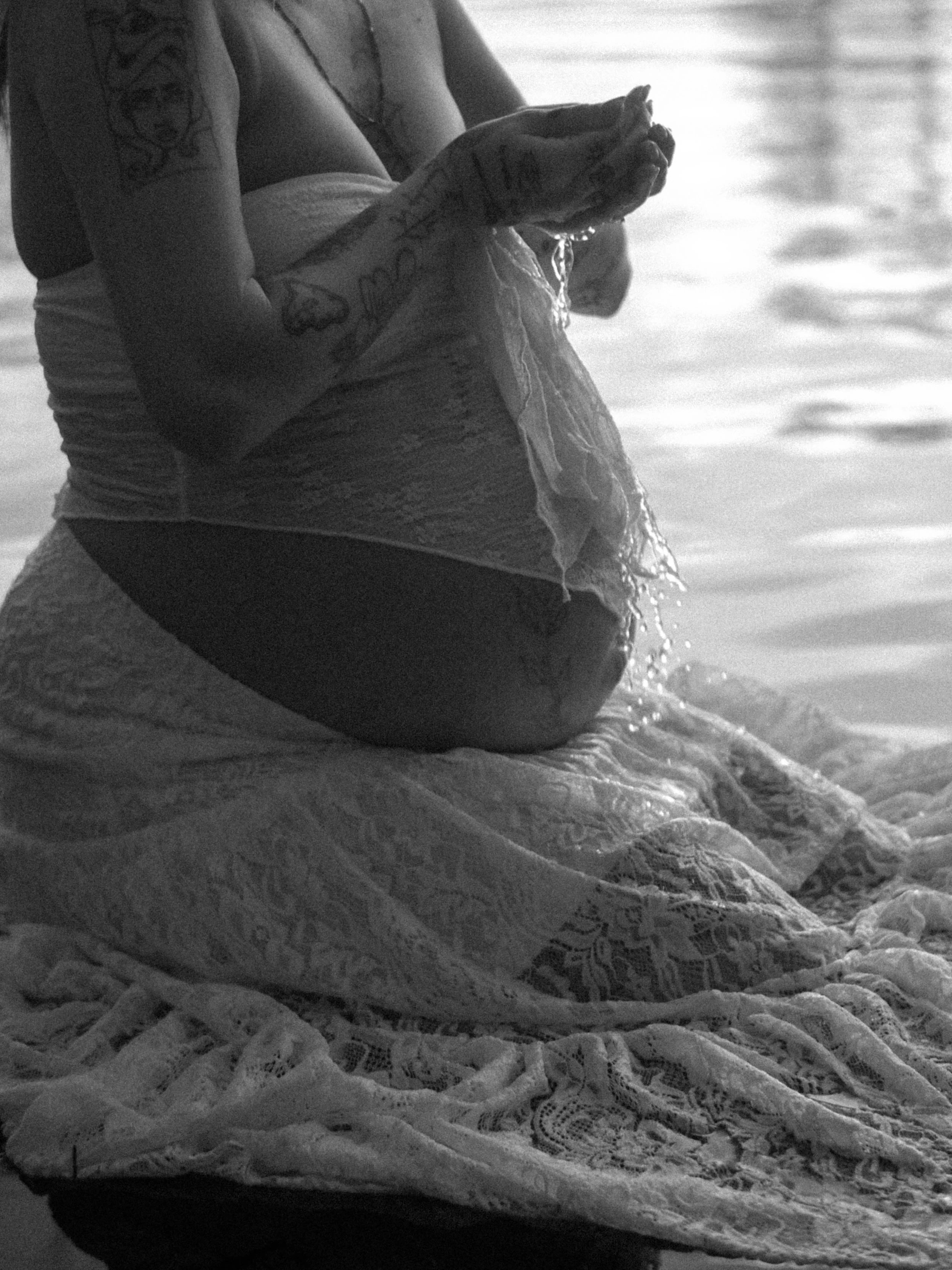 A person holding a lace cloth or towel near a body of water in black and white.