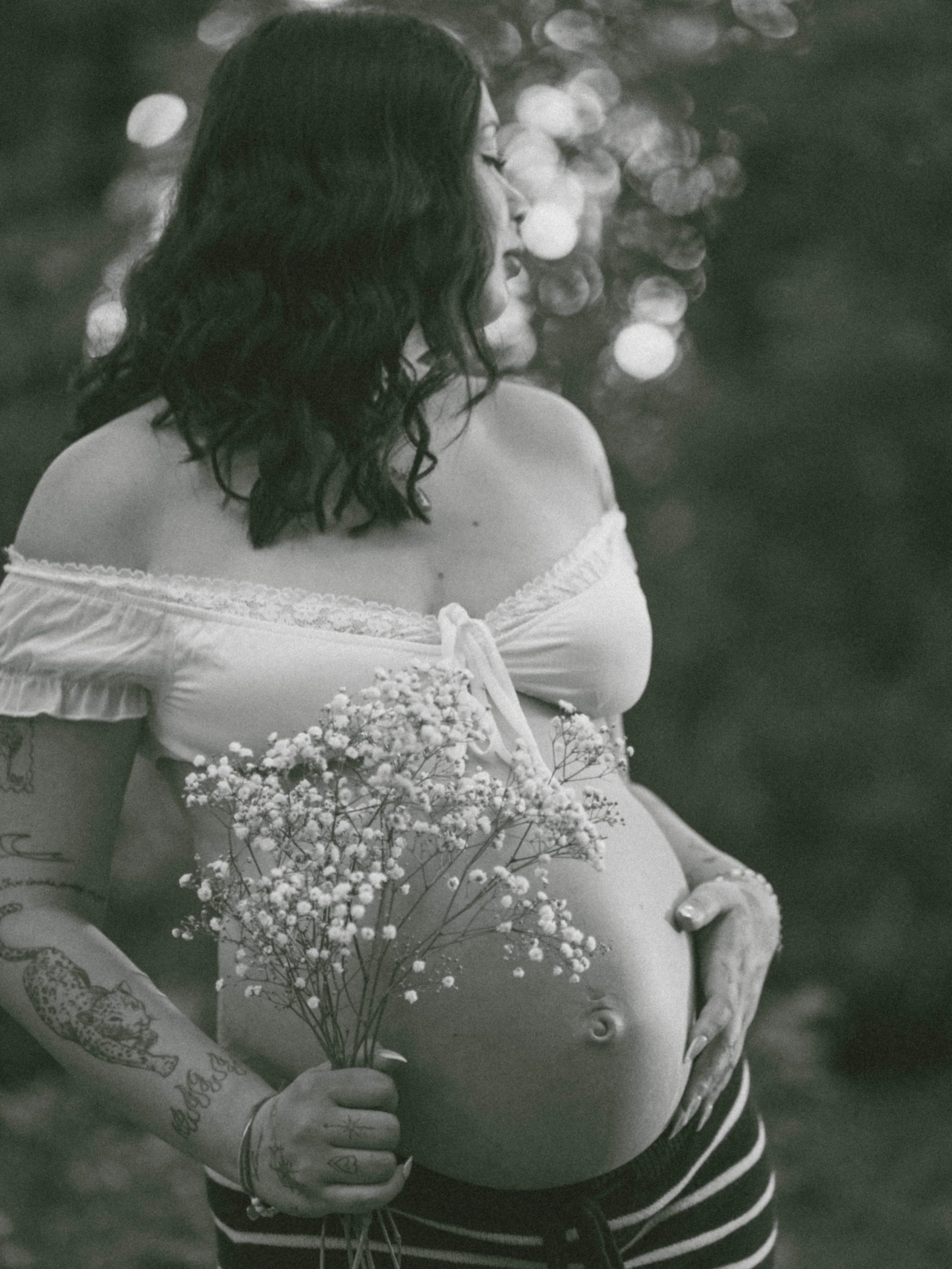 A pregnant woman holding a bouquet of small white flowers, with her hand resting on her belly, seen from the side in black and white.