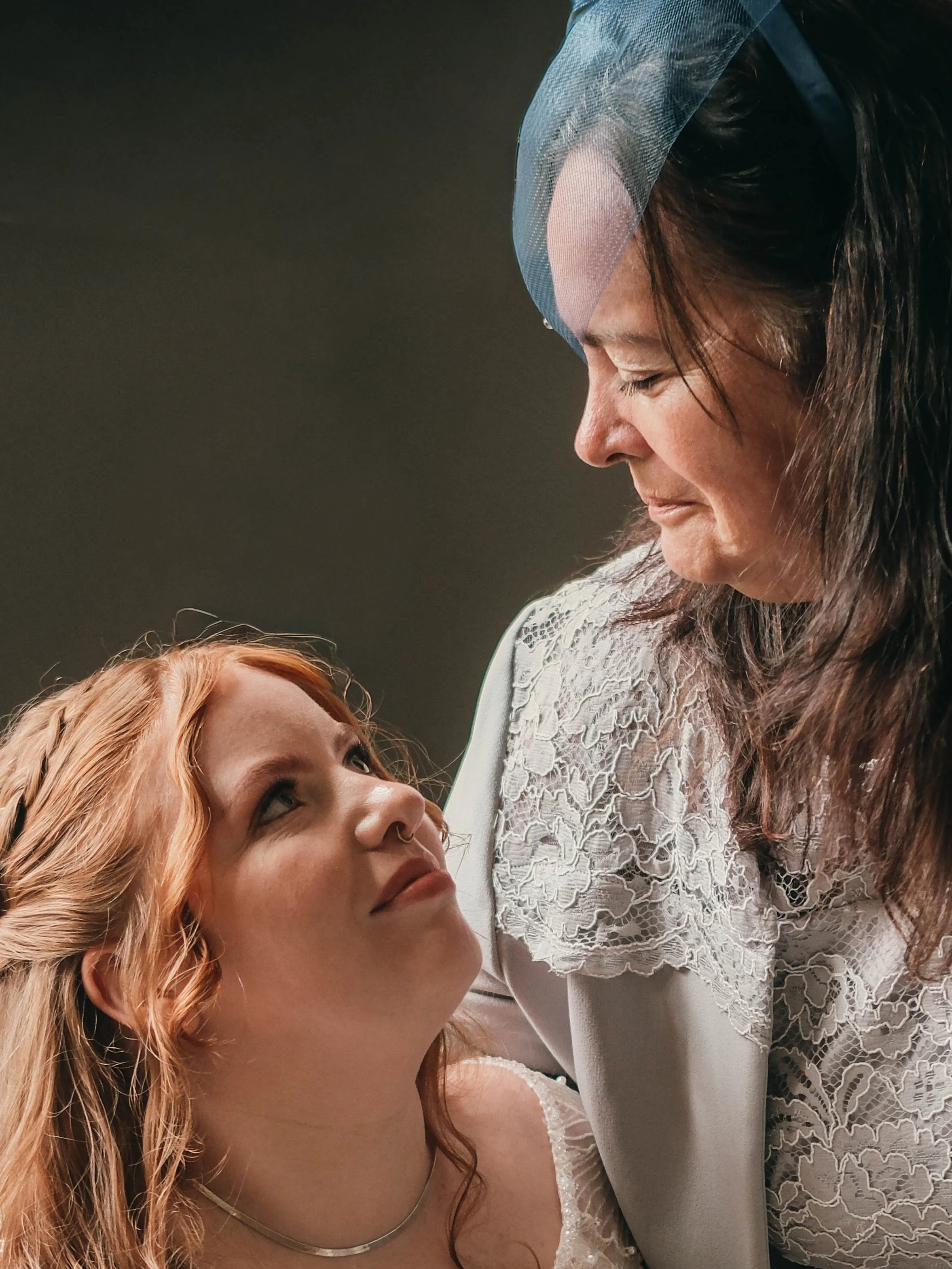 A woman with long dark hair wearing a lace top and a bidet reaching out to a young girl with ginger hair, blue eyes, and a nose ring, with both sharing a quiet moment.
