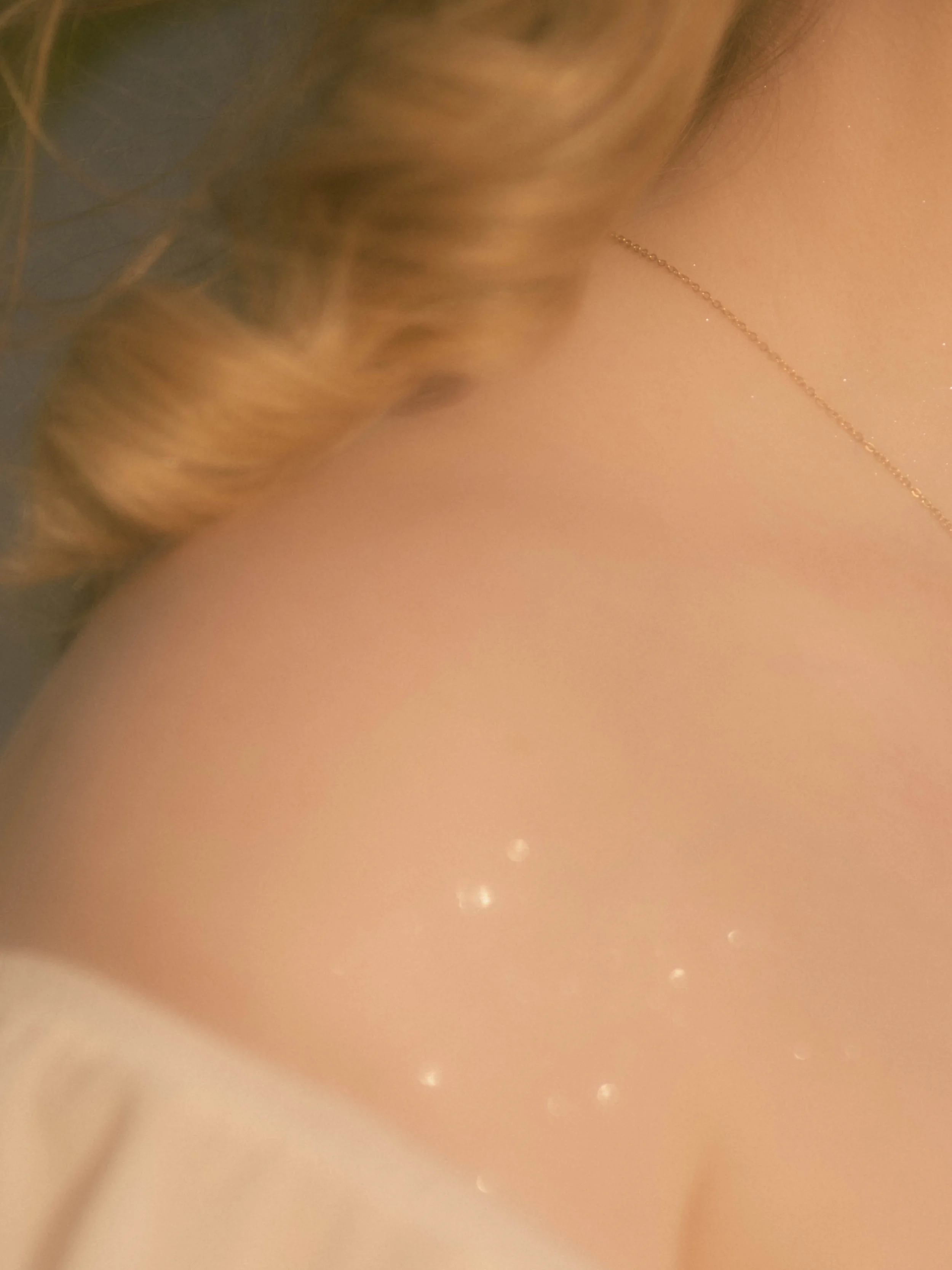 Close-up of a person's shoulder with blonde hair and a delicate gold necklace.