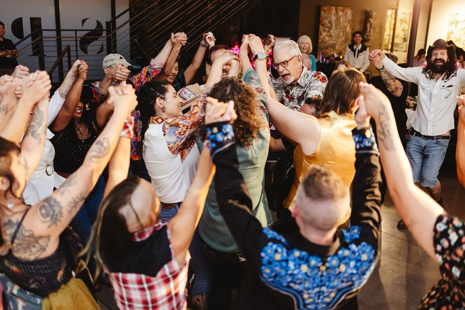 A group of people dressed in "queer cowboy" attire holding hands and pushing into the middle of a circle