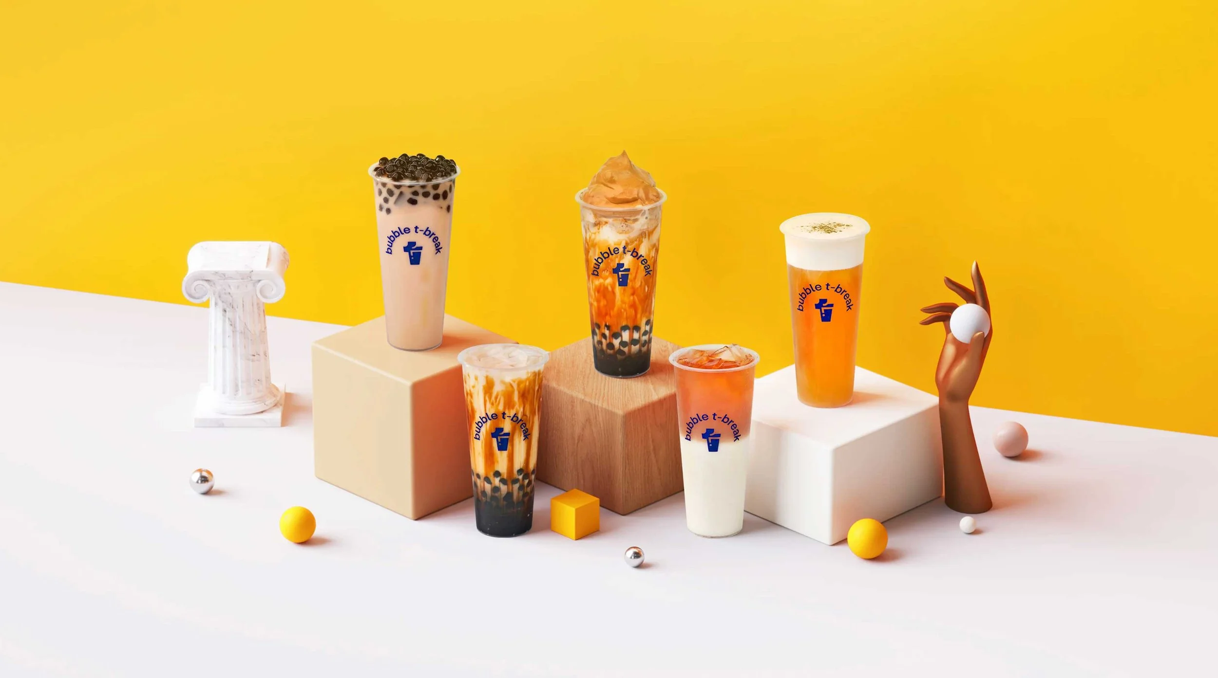 Assorted bubble tea drinks with tapioca pearls and toppings displayed on a white surface against a yellow background, decorated with small colorful spheres, cubes, and a classical column miniature.