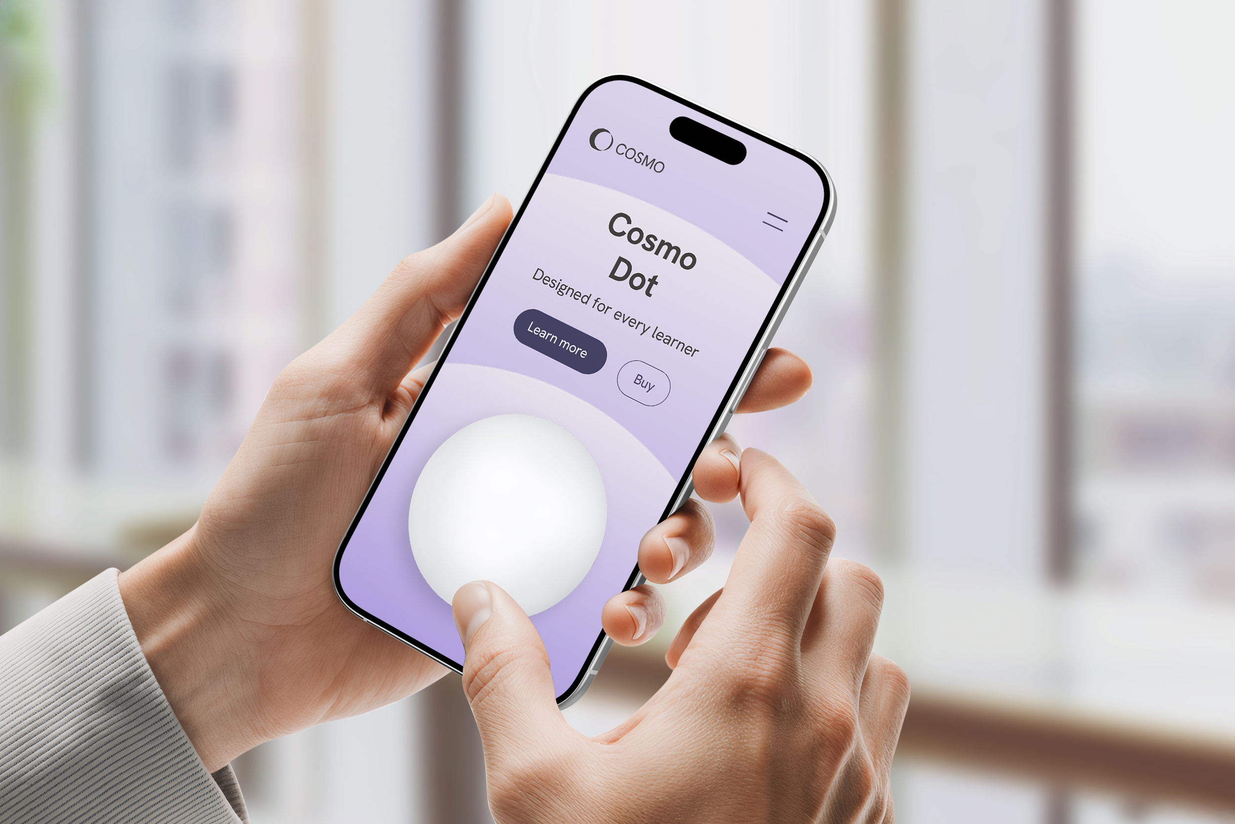 Hand holding a smartphone displaying an app for 'Cosmo Dot,' with a large white dot and options to learn more or buy, set against a blurred background with windows.