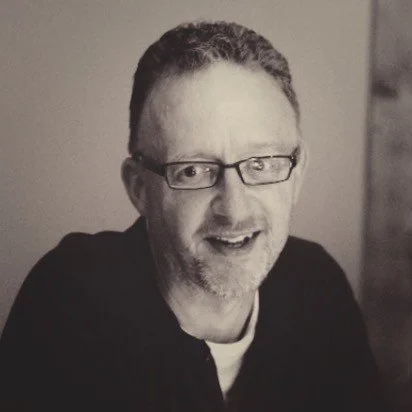 Black and white portrait of a smiling man with glasses and a short beard.