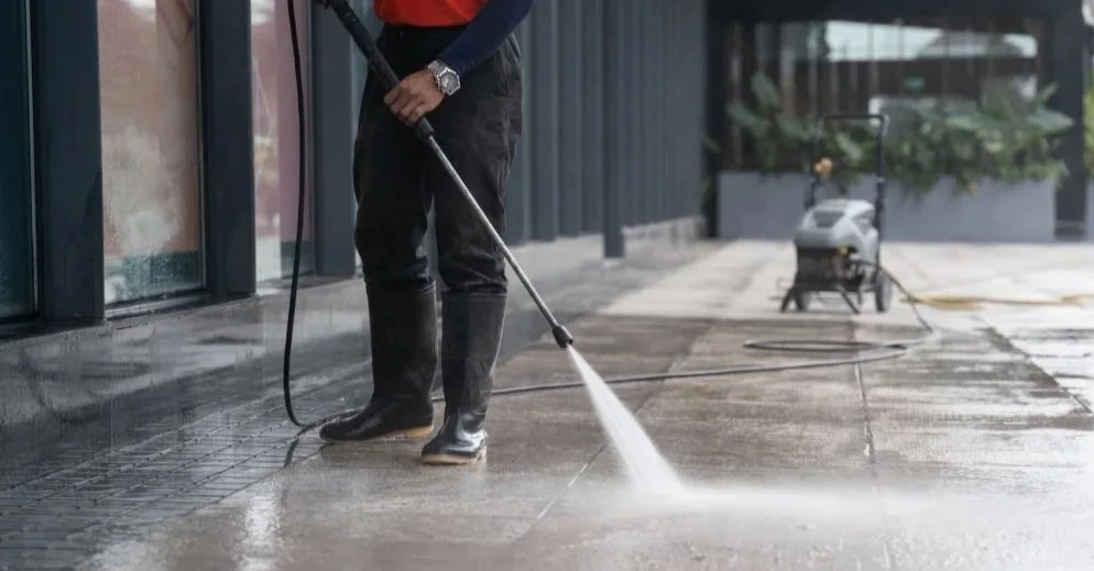Person in black rubber boots power washing a concrete sidewalk.