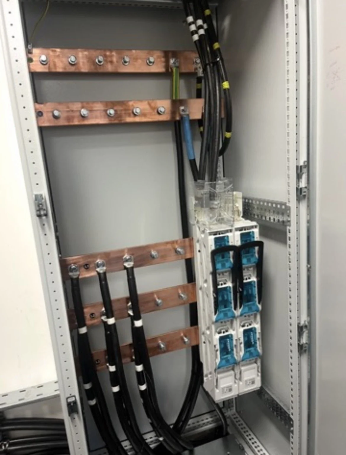 Electrical panel with black cables, circuit breakers, and copper bus bars inside a metal enclosure.