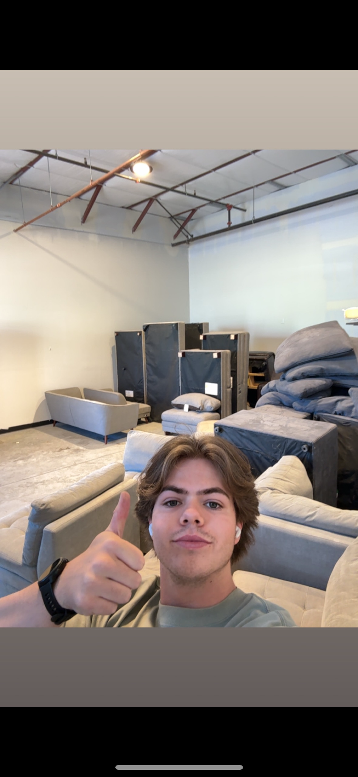 Young man taking a selfie in an industrial storage area with furniture and stacked foam padding.