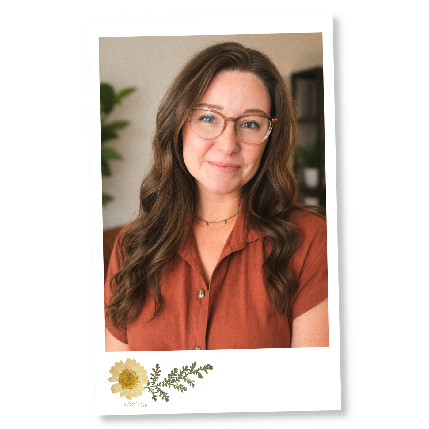 Photograph of a woman with long brown hair, wearing glasses, and an orange-brown shirt, smiling softly at the camera. In the background, blurred bookshelf and green plant. The picture has a floral design with a daisy and green leaves along with an inscription "5/19/2026"