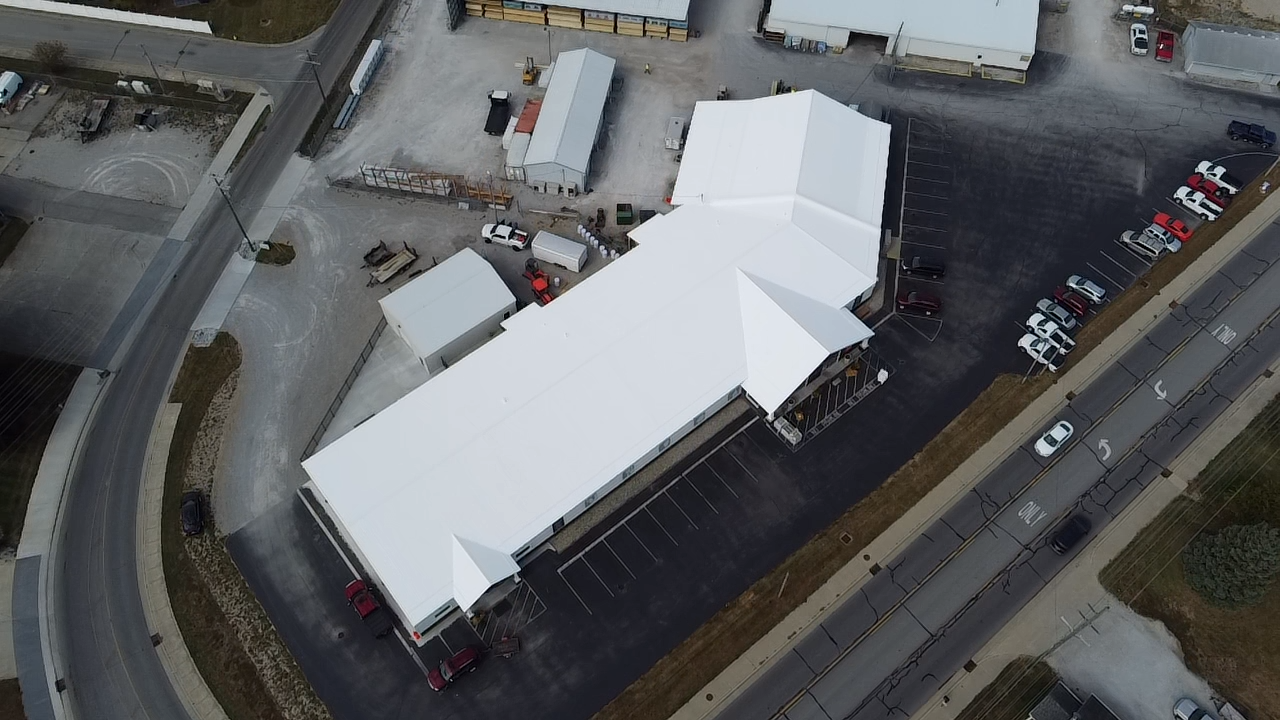 An aerial view of a large building with a white roof, parking lot, and surrounding roads.