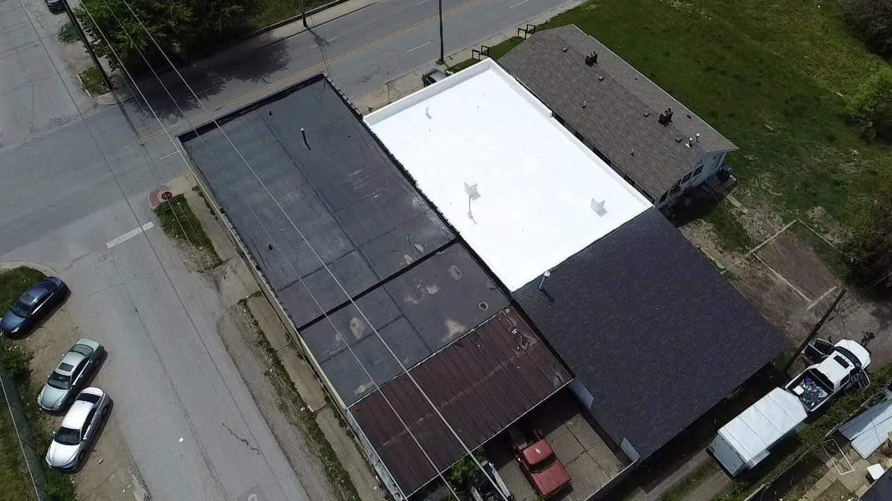 Aerial view of a building with three different roof sections: one black, one white, and one reddish-brown, along with surrounding parked cars and streets.