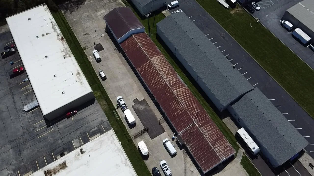 Aerial view of an outdoor parking lot with several buildings, parked cars, and vans.
