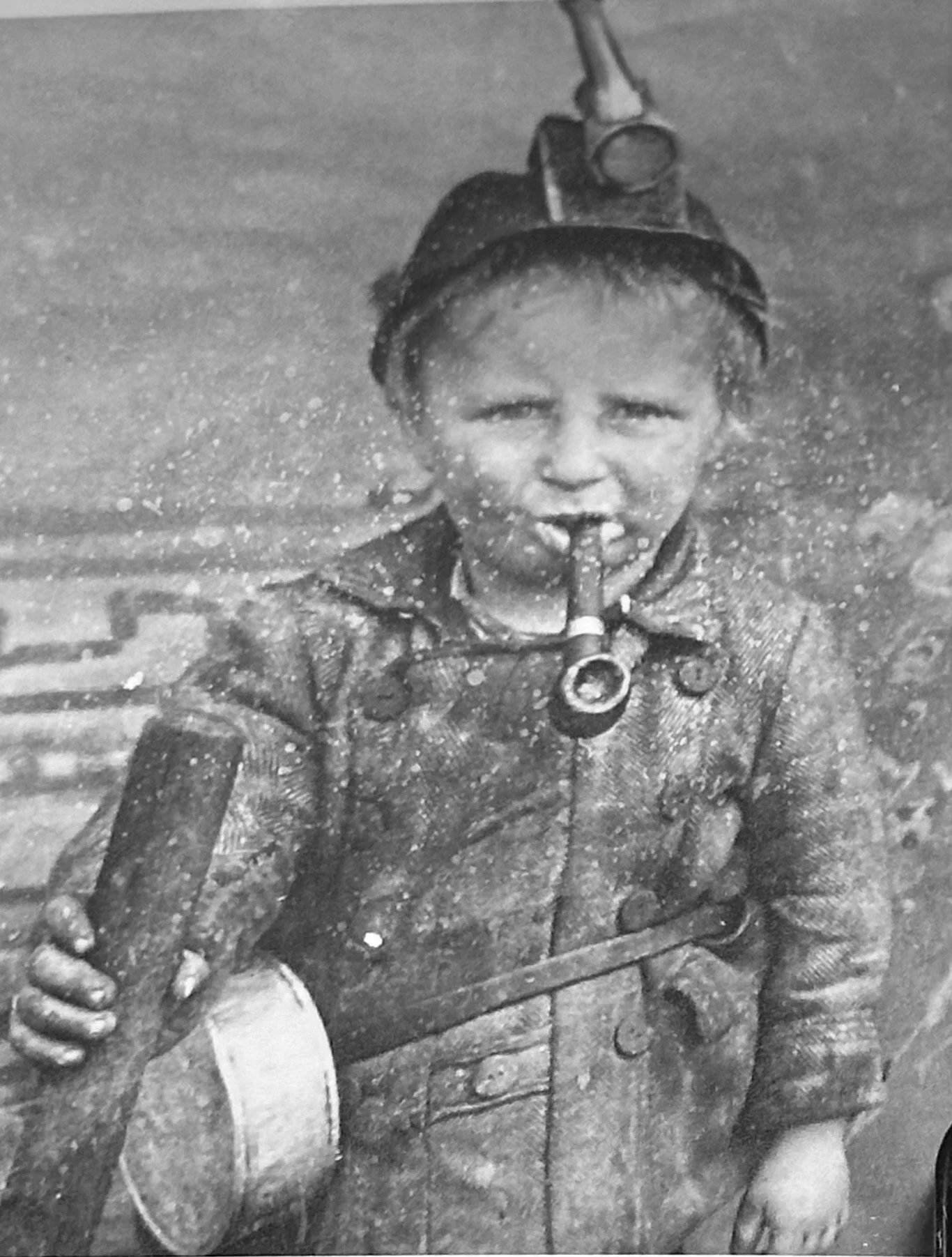 A young boy in a jacket, holding a guitar, and standing in the water.
